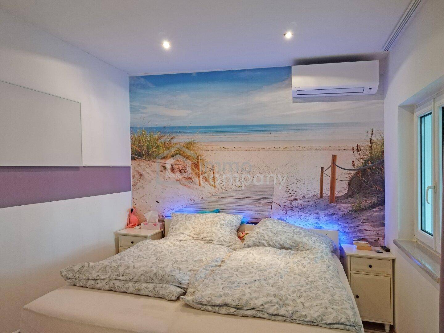 Schlafzimmer mit Doppelbett, Strandtapete als Akzentwand und Klimaanlage für angenehmes Klima.