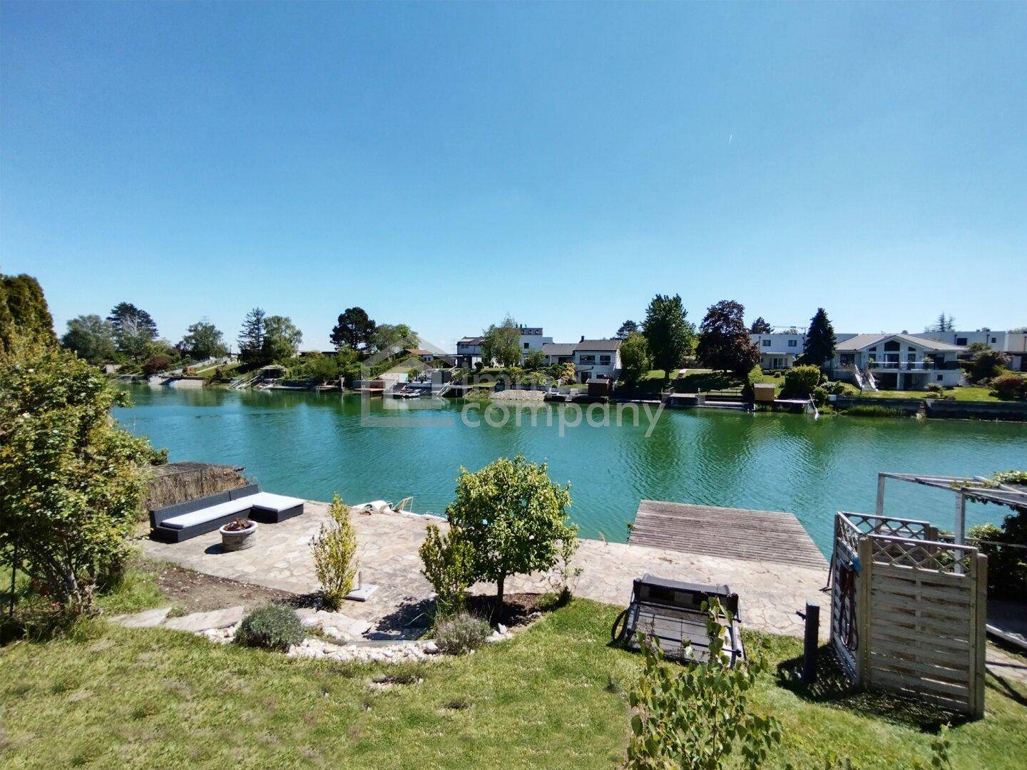 Weitläufiger Gartenbereich mit direktem Zugang zum See und Blick auf die gegenüberliegenden Häuser.