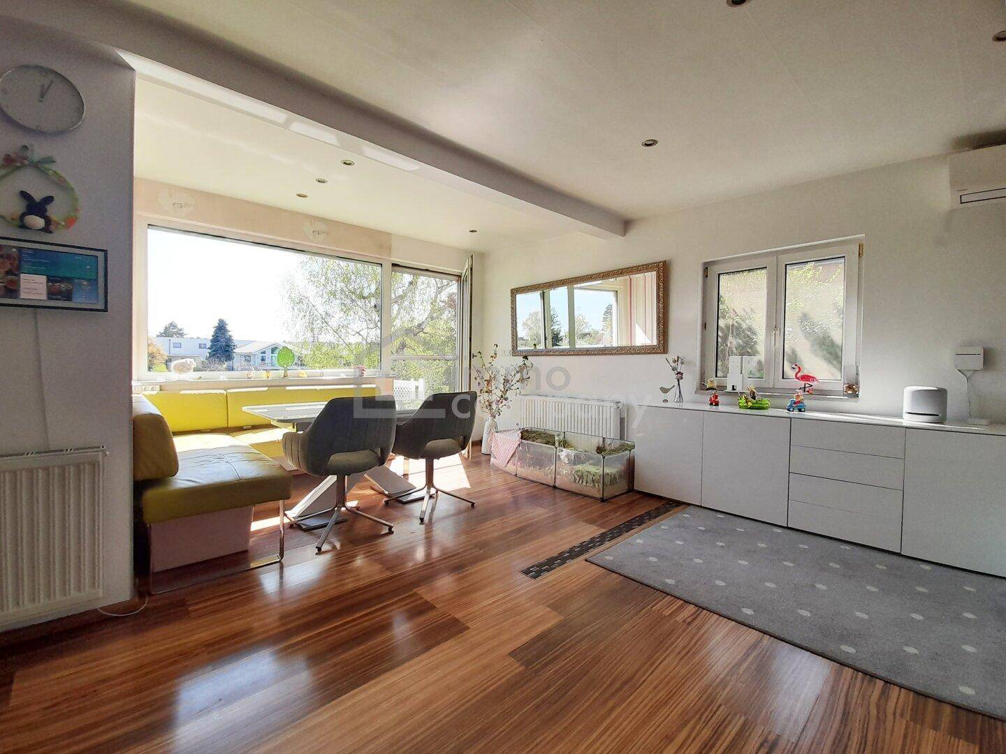 Heller Wohn- und Essbereich mit großen Fenstern, Holzboden und modernem Sideboard.