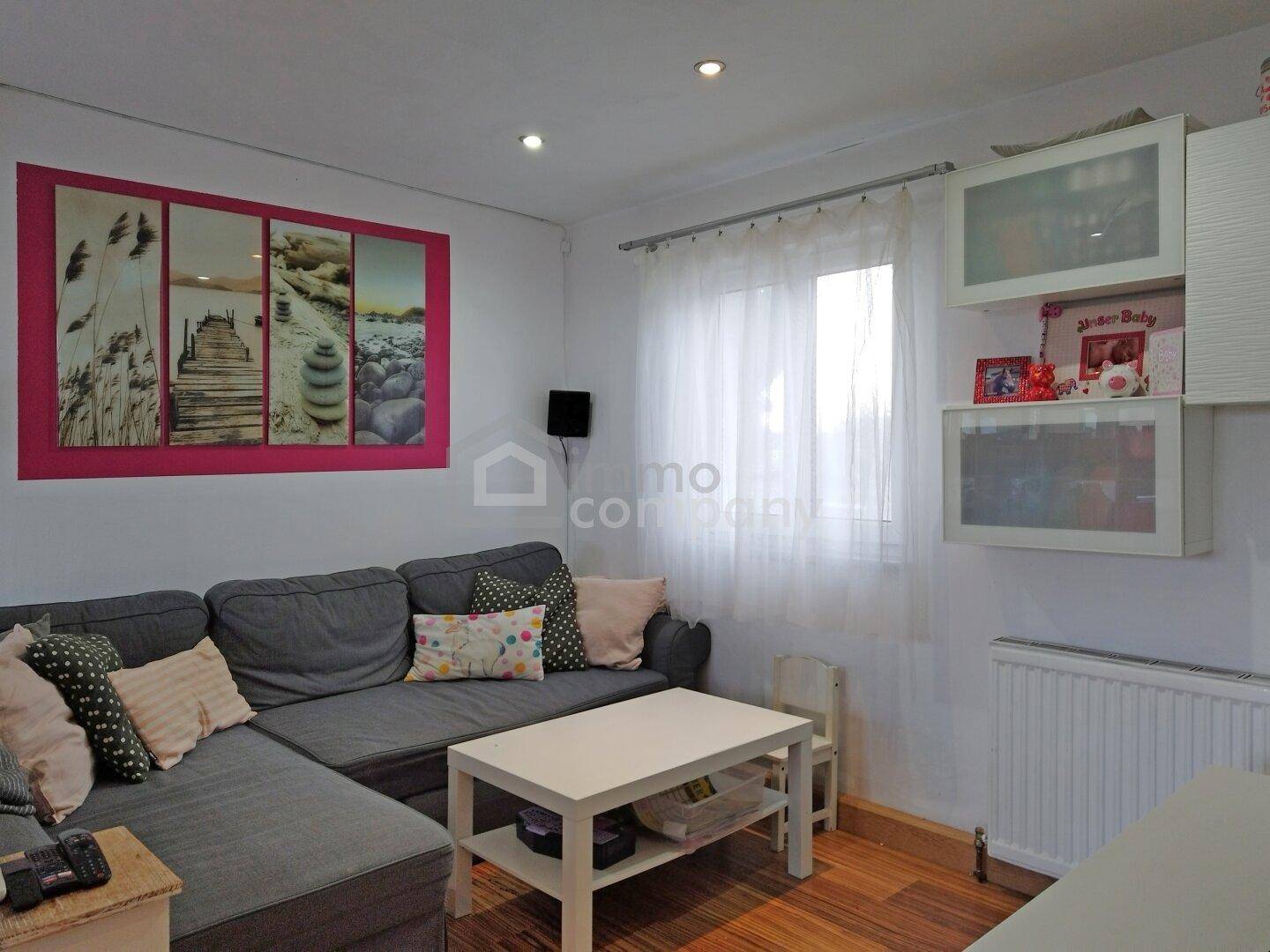 Gemütliches Wohnzimmer mit großem Ecksofa, hellem Couchtisch und Fenster mit Vorhängen.