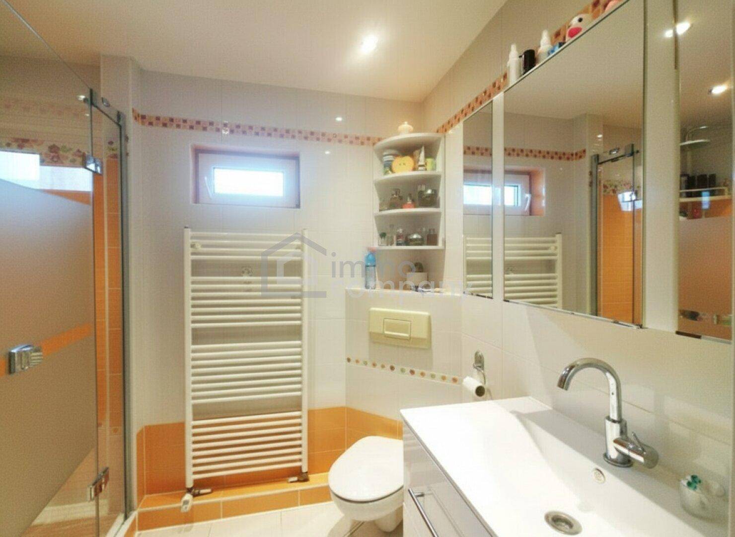 Modernes Badezimmer mit orange-weißen Fliesen, Dusche, WC und beheiztem Handtuchhalter.