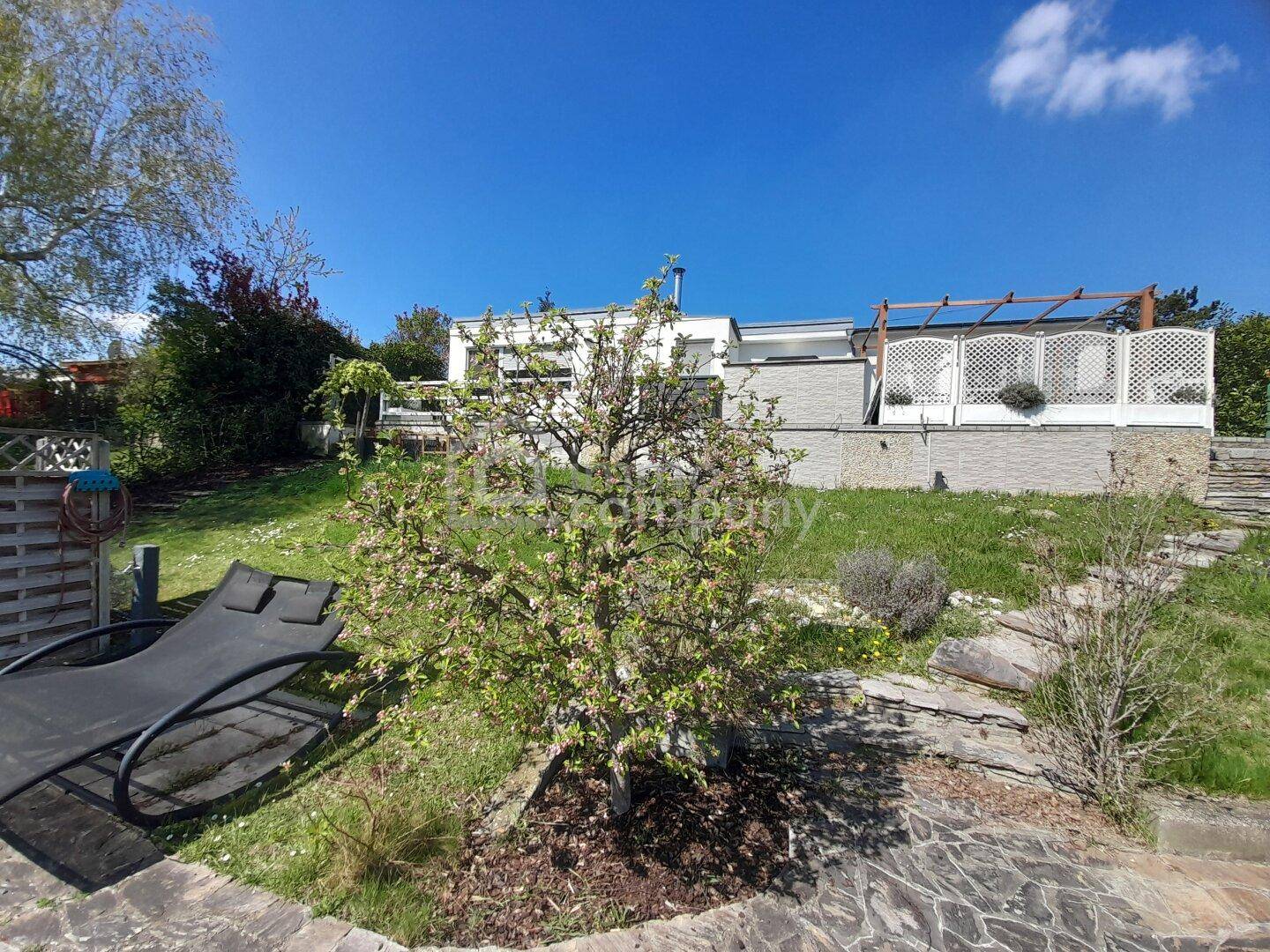 Gepflegter Gartenbereich hinter dem Haus mit Liegestuhl, Rasenfläche und blühenden Bäumen.