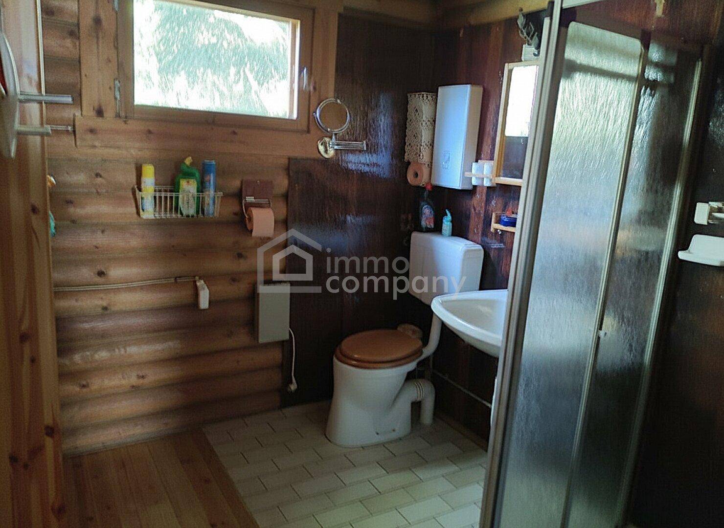 Badezimmer mit Holzwänden, Fliesenboden, Toilette, Waschbecken und Duschkabine.