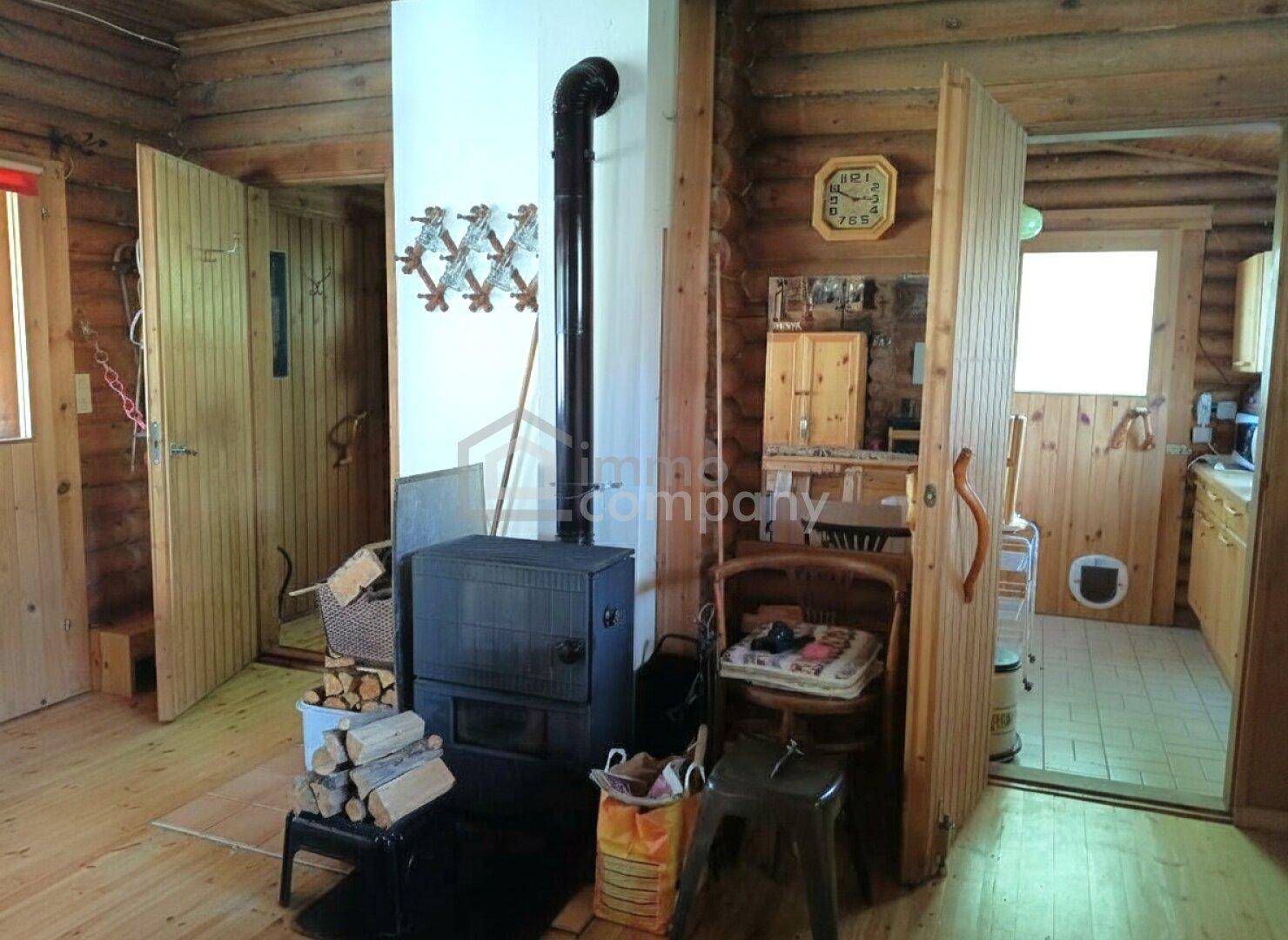 Rustikaler Wohnbereich mit einem Holzofen und Holzböden, umgeben von Blockwänden.