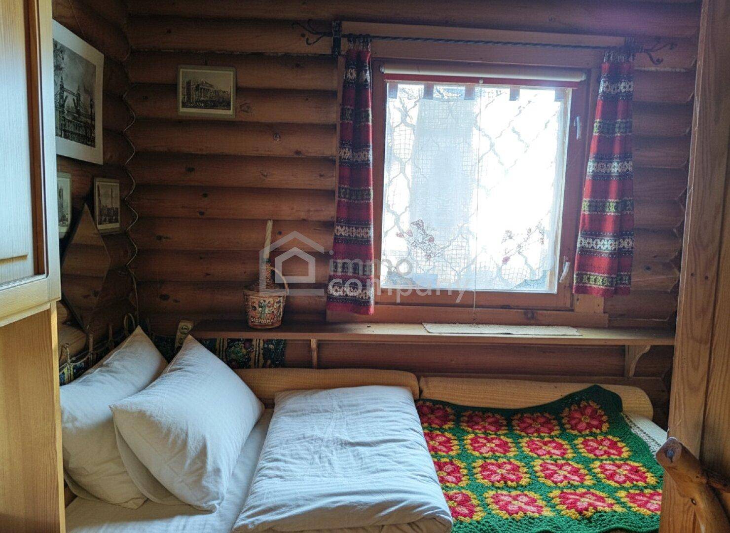 Kleines Schlafzimmer mit Holzwänden, einem Fenster und traditionellen Vorhängen.