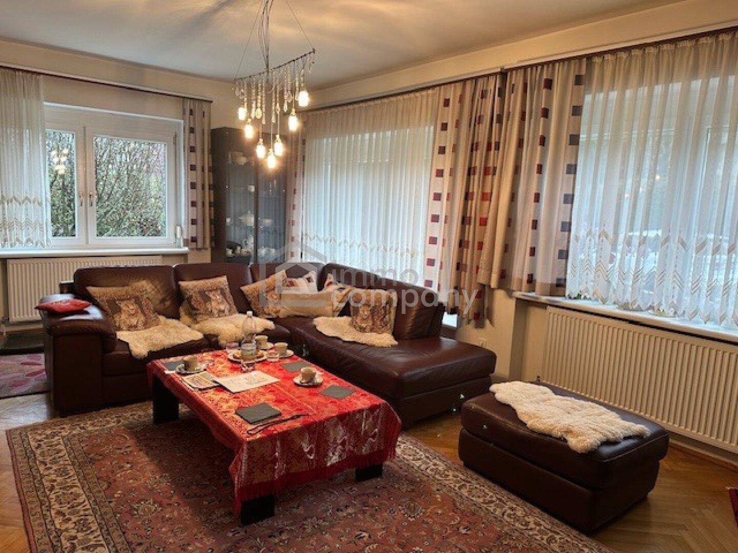 Gemütliches Wohnzimmer mit Ledersofa, Teppich und Fenstern mit Vorhängen.