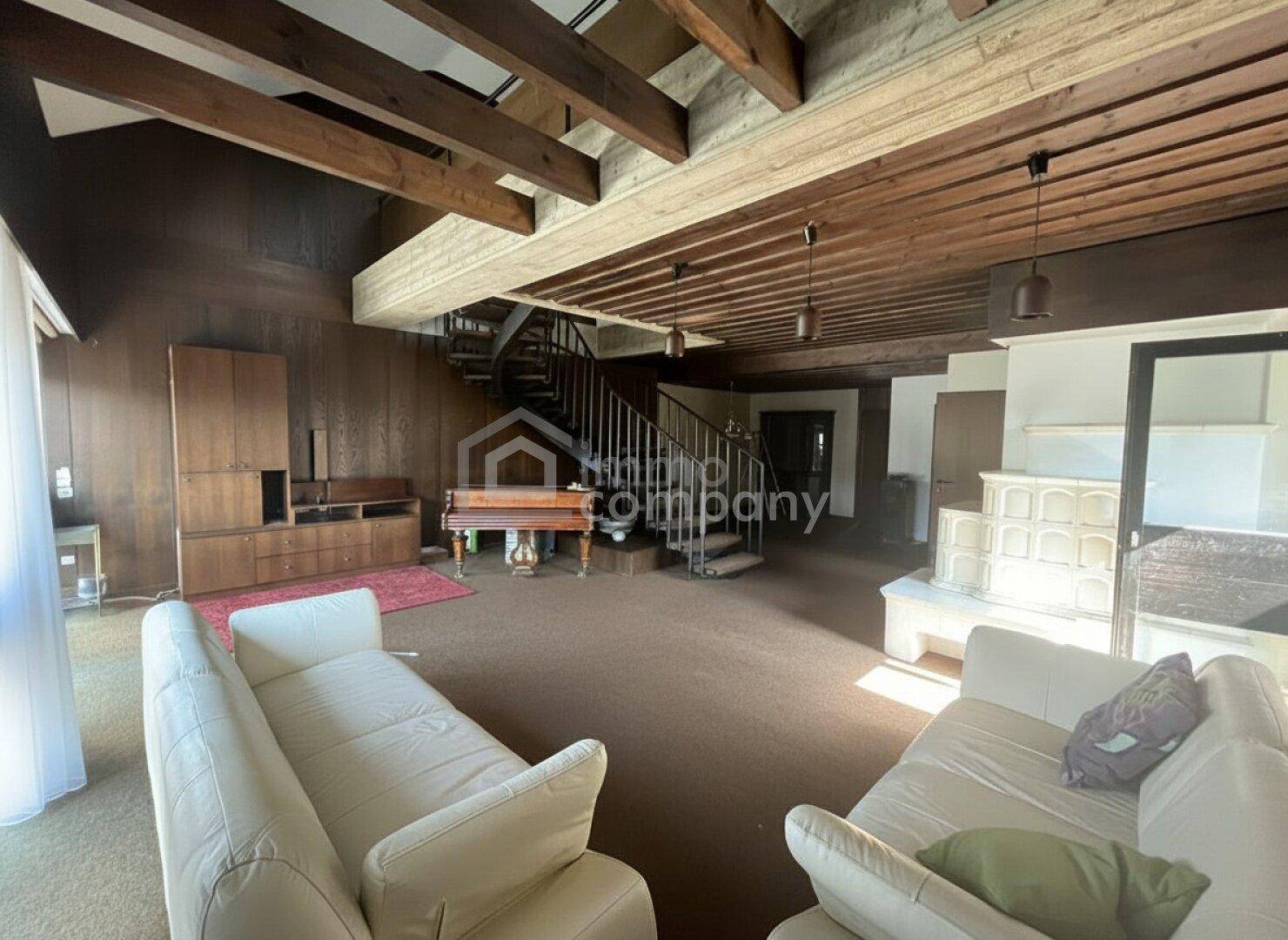 Geräumiges Wohnzimmer mit Holzbalkendecke, Kachelofen und Wendeltreppe.