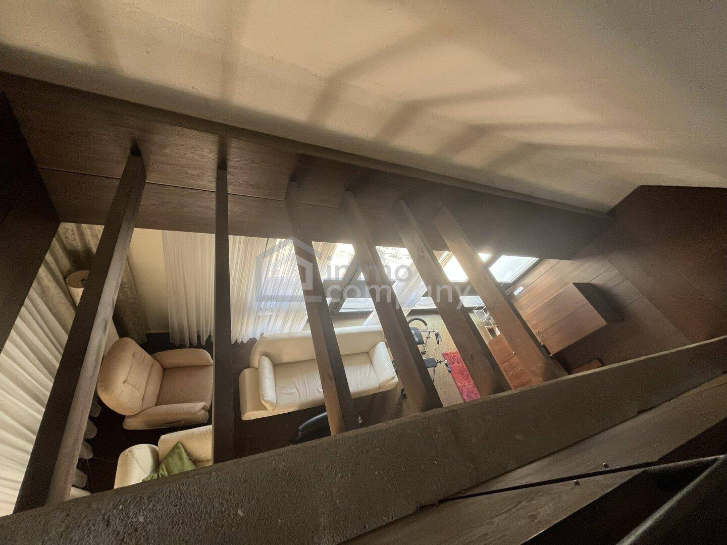 Blick von der Treppe in einen Wohnbereich mit hellen Sofas und Vorhängen.
