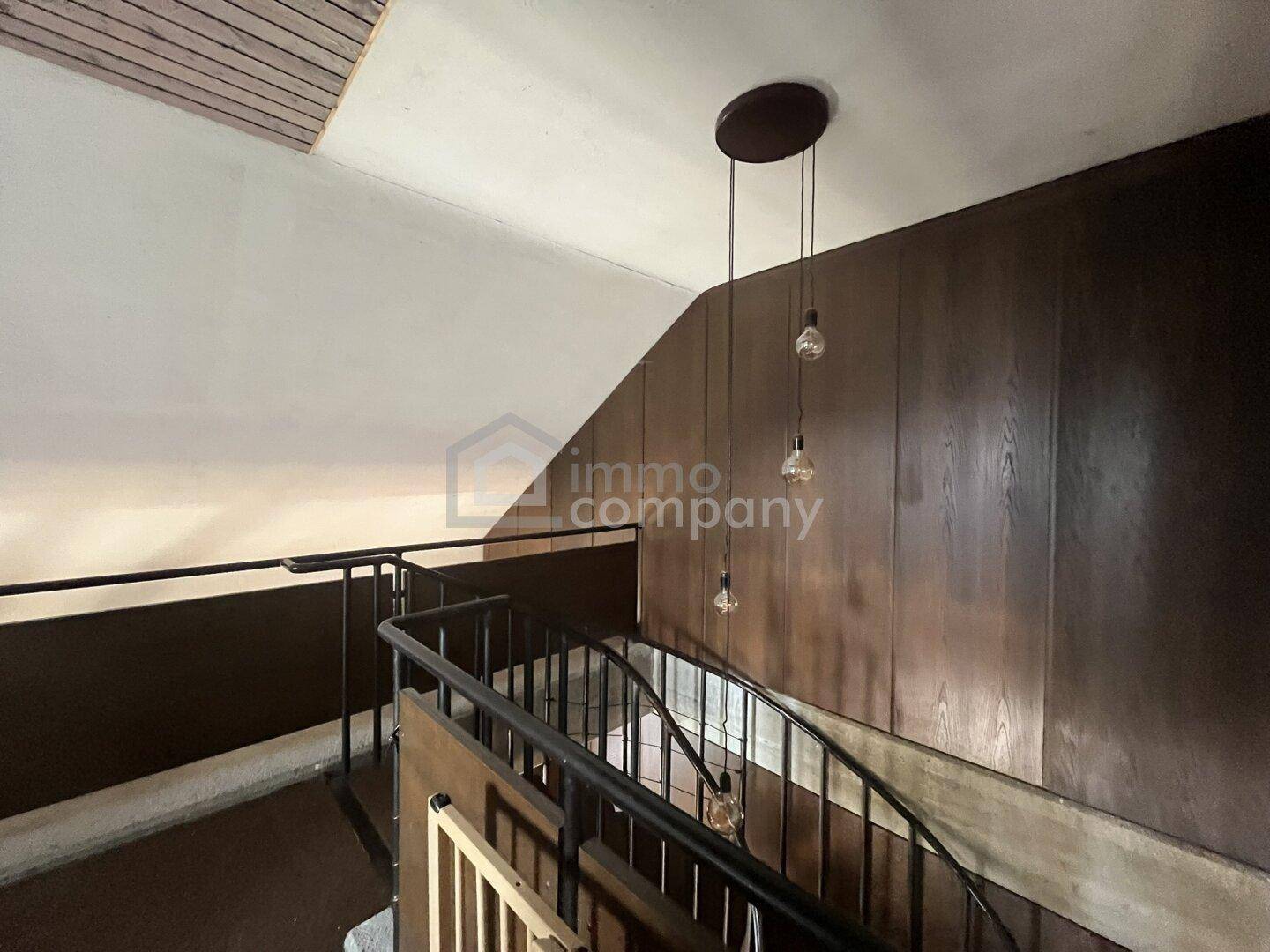 Wendeltreppe mit dunklem Holzgeländer und dekorativer Hängelampe.
