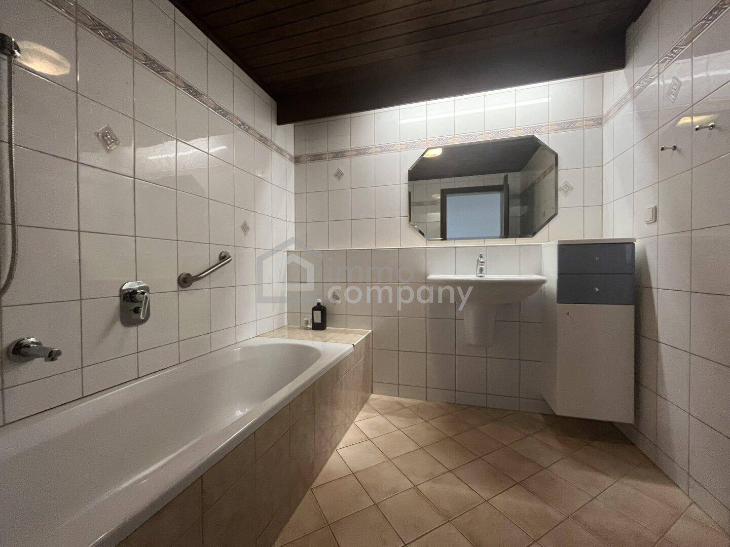 Badezimmer mit Badewanne, Waschbecken und weißen Fliesen im 80er-Jahre-Stil.