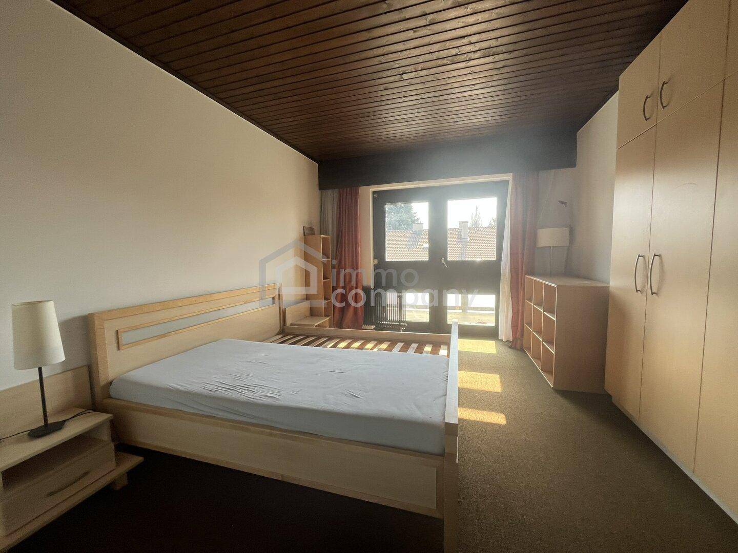 Schlafzimmer mit Holzbett, Kleiderschrank und Zugang zu einem Balkon oder Terrasse.