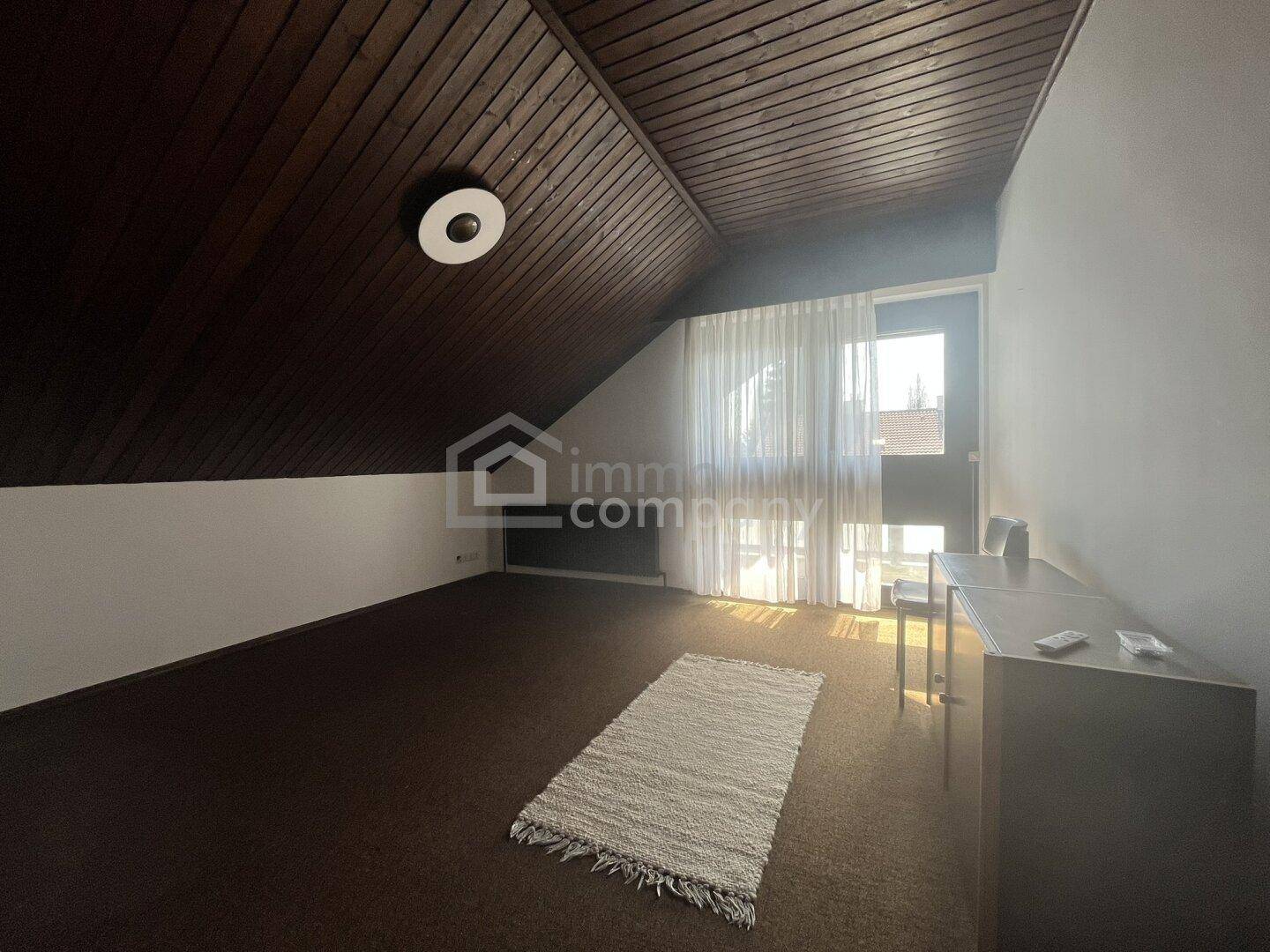 Dachzimmer mit schräger Decke, Holztäfelung und Fenster für natürliches Licht.