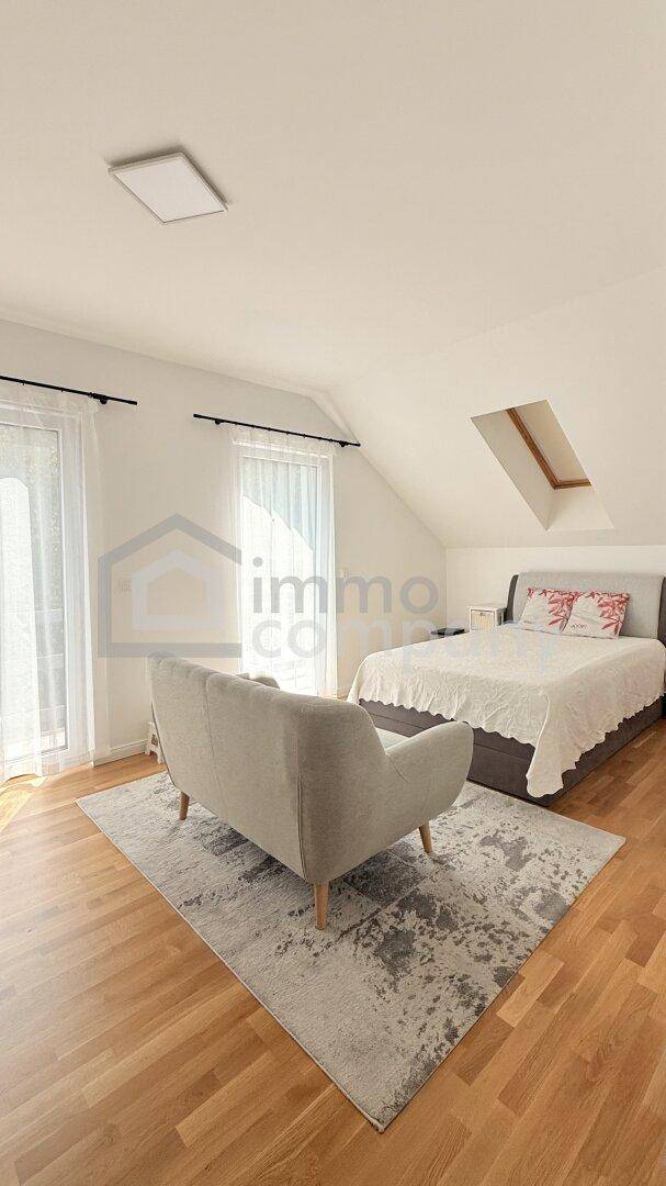 Helles Schlafzimmer im Dachgeschoss mit Dachfenster, Sofa und Holzboden.