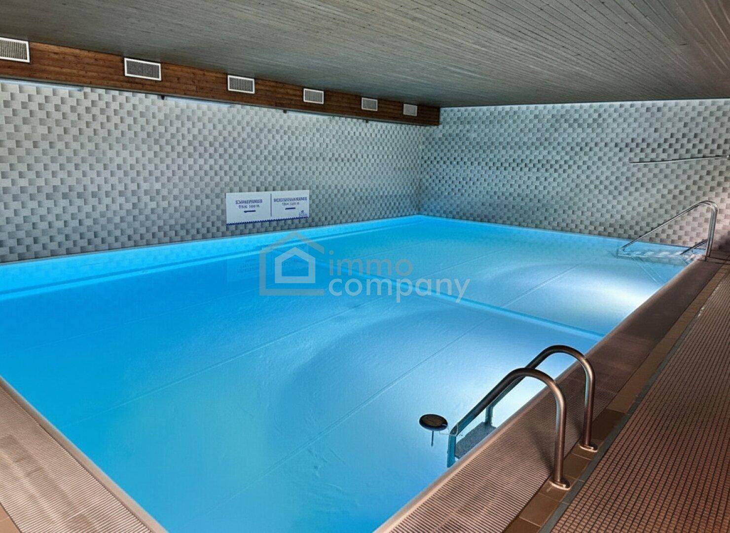 Großes Hallenbad mit blauer Beleuchtung und gefliesten Wänden für sportliche Aktivitäten.
