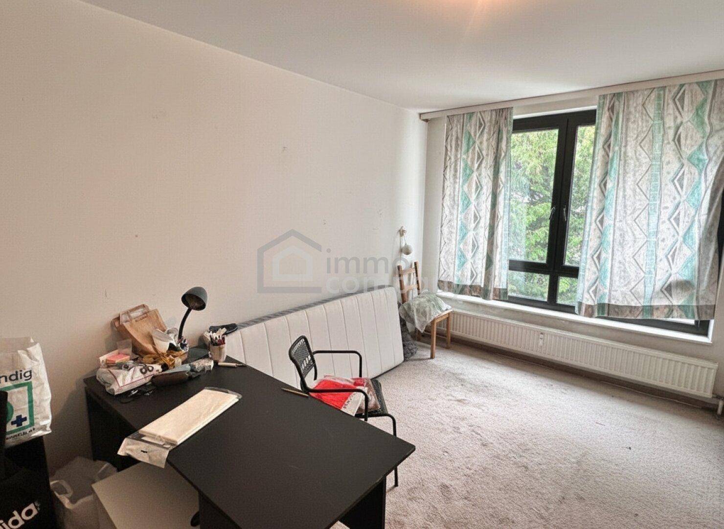 Schlafzimmer mit Teppichboden, großem Fenster und einem Schreibtisch.