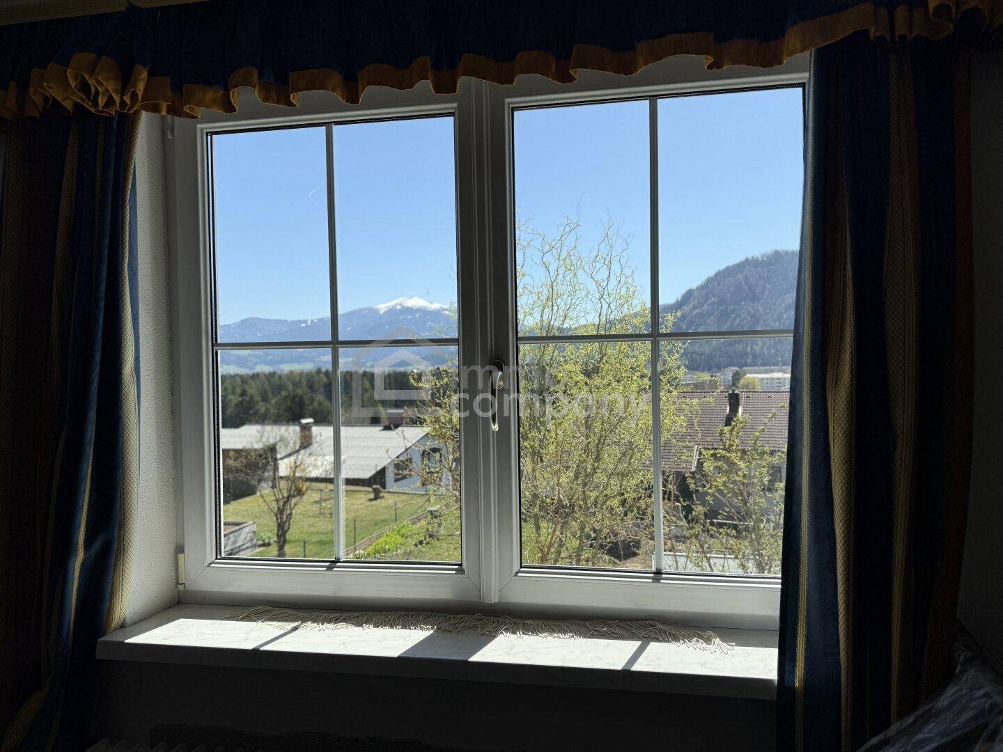 Fensterblick auf die umliegende Landschaft mit Bergen und grünen Wiesen.