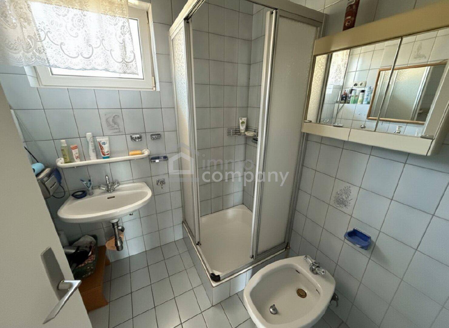 Badezimmer mit Dusche, Waschbecken, Bidet und hellblauen Fliesen.
