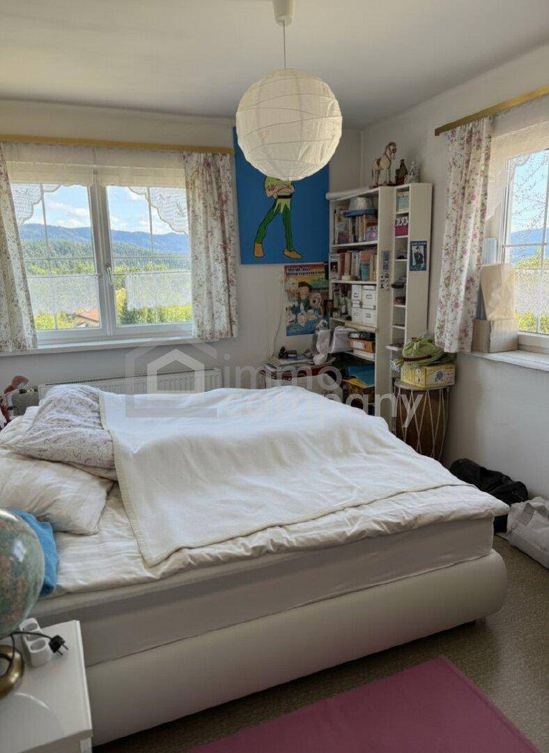 Kinderzimmer mit hellem Bett, Bücherregal und Fenstern mit Blick ins Grüne.