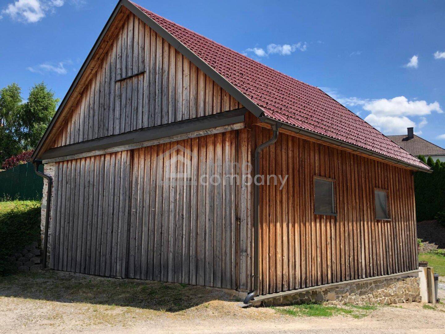 Rustikales Holzgebäude mit rotem Ziegeldach und vertikaler Holzverkleidung unter blauem Himmel.