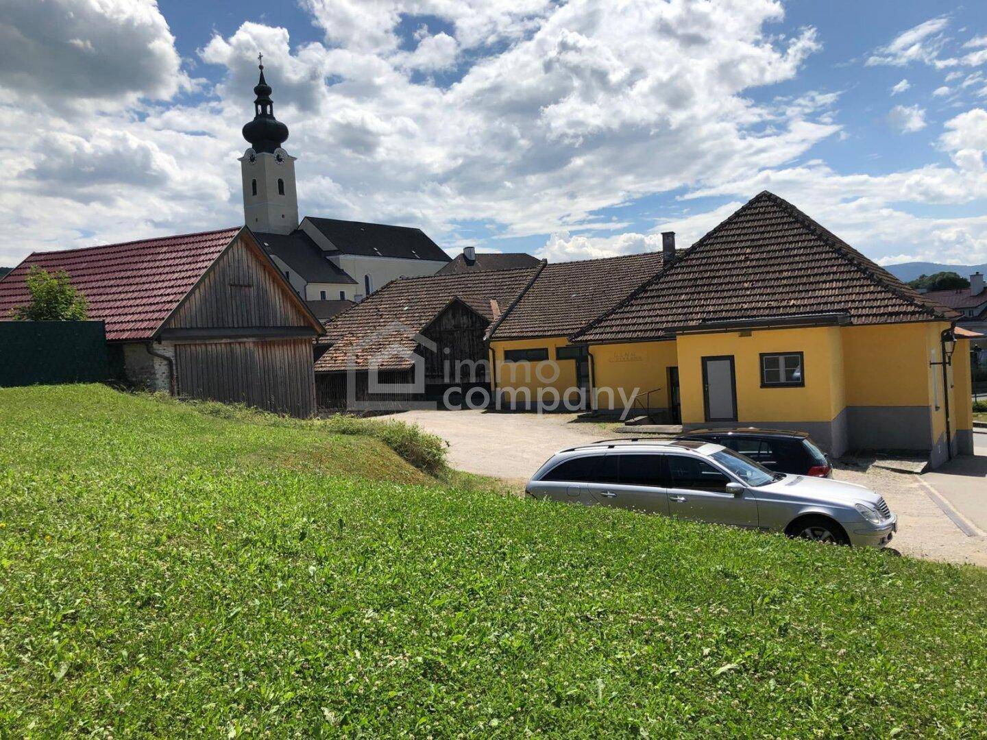 Panoramablick auf das Anwesen mit umliegenden Gebäuden und einer Kirche im Hintergrund.