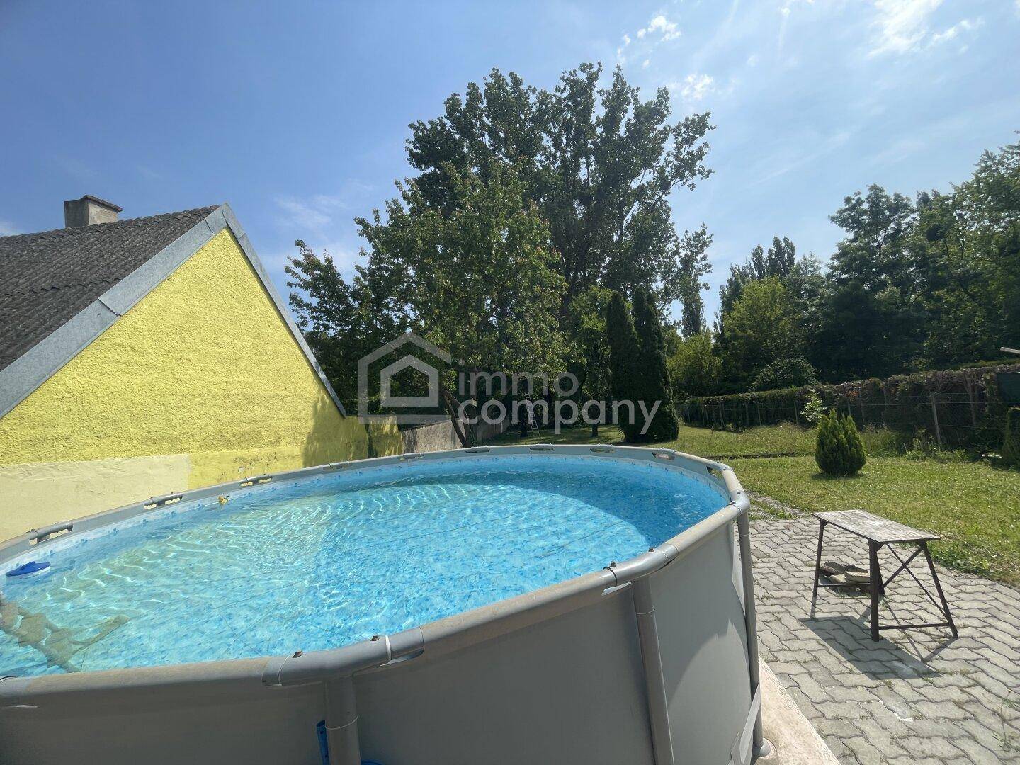 Hinterhof mit einem Aufstellpool, gepflastertem Bereich und viel Grün.