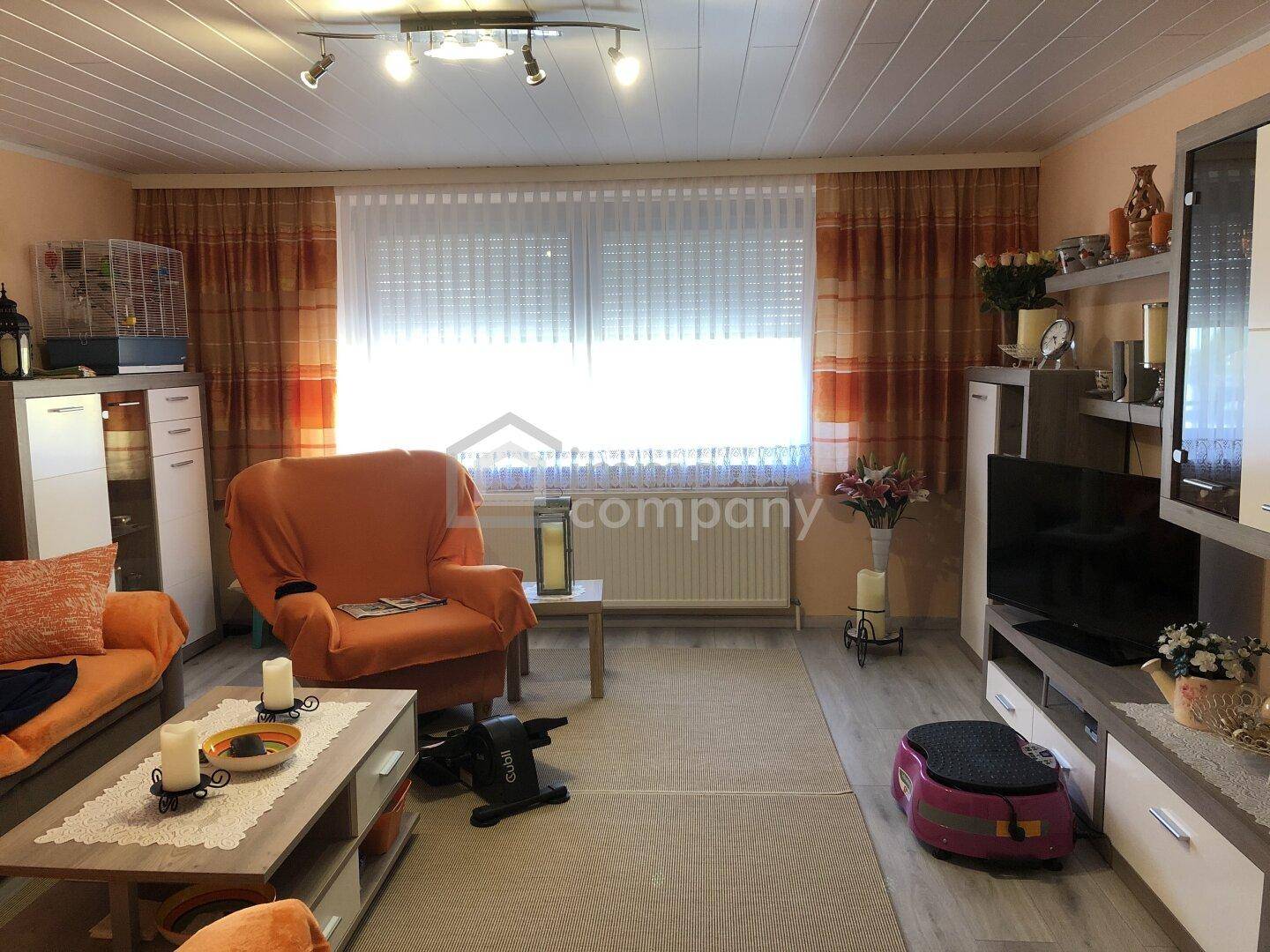 Wohnzimmer mit bequemen Sitzgelegenheiten, einem Fernsehmöbel und einem großen Fenster.