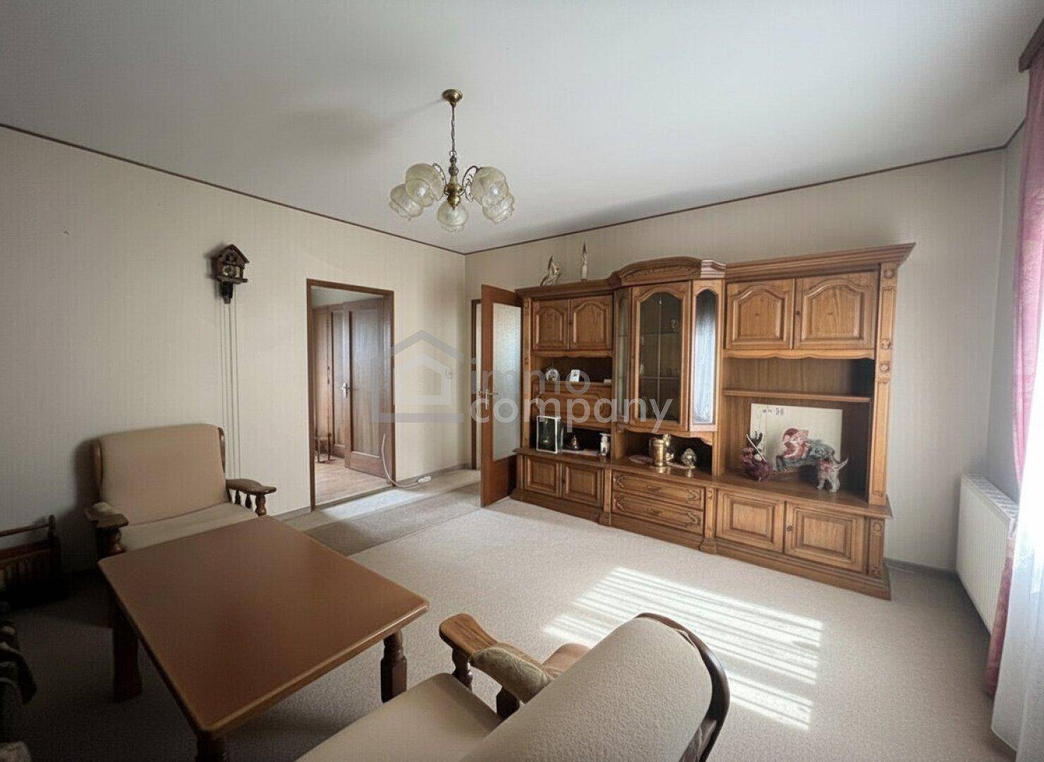 Geräumiges Wohnzimmer mit traditionellen Holzmöbeln, Teppichboden und Kronleuchter.
