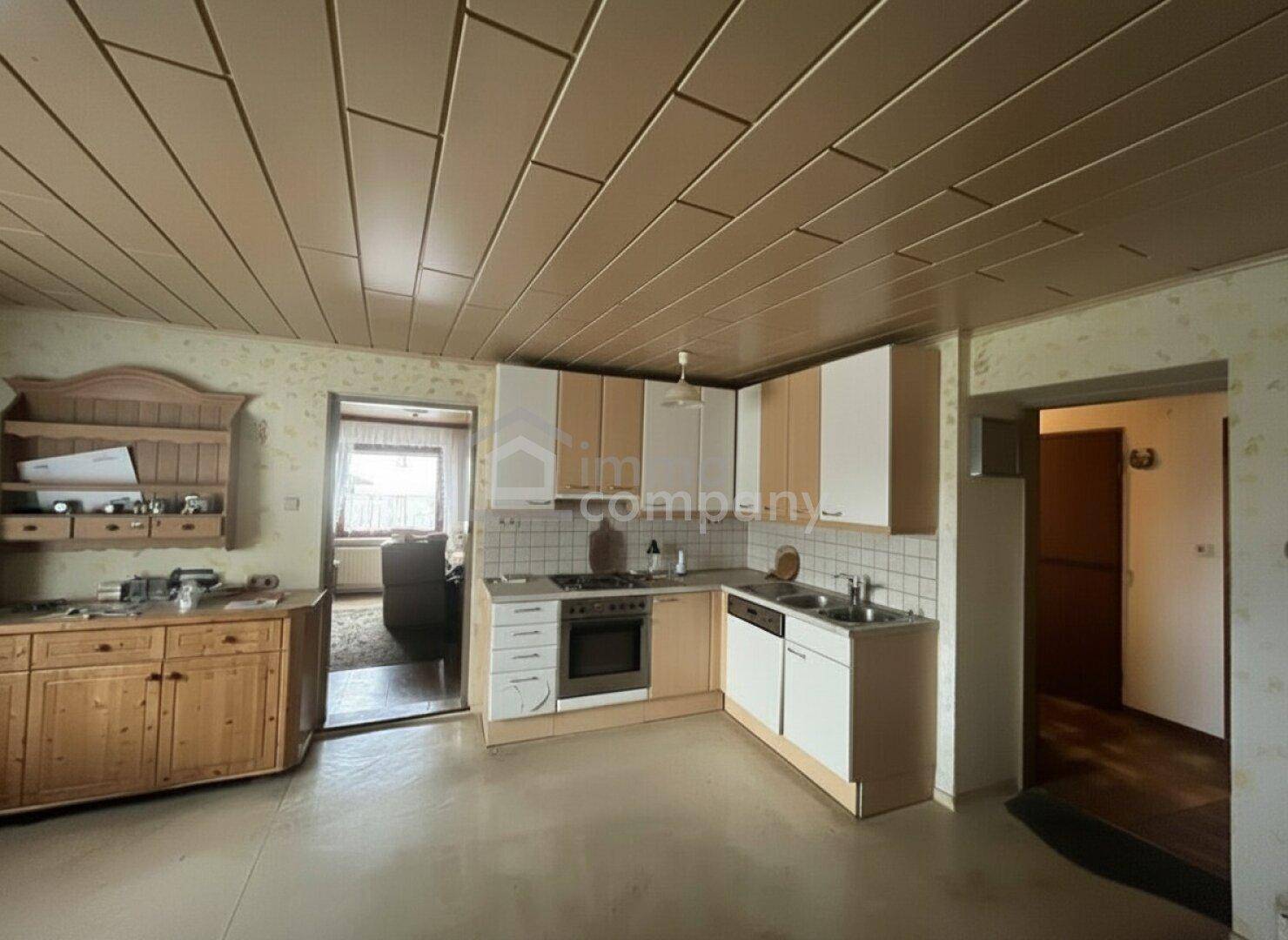 Küche mit hellen Holz- und weißen Schränken, Herd und Spüle, sowie Holzdeckenverkleidung.