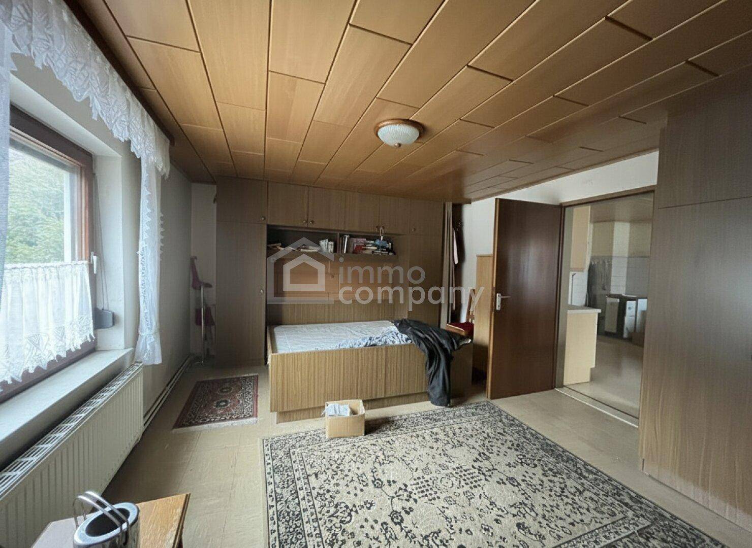 Schlafzimmer mit Einzelbett, Einbauschränken, Fenster und Holzdeckenverkleidung.