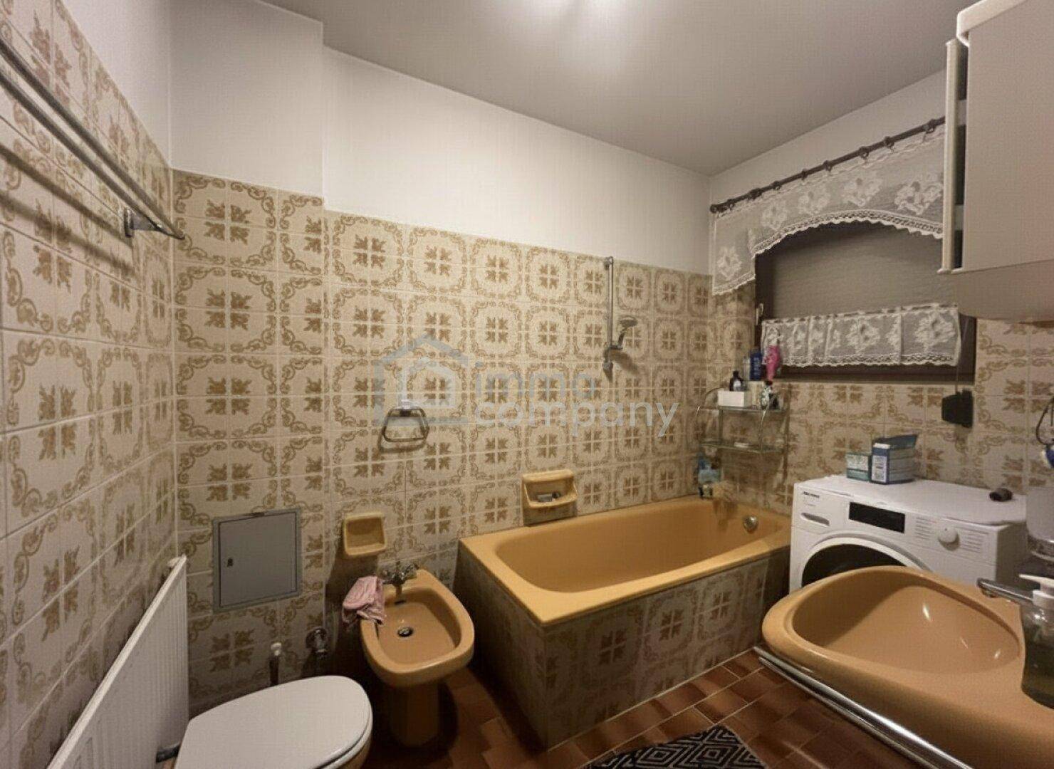Badezimmer im 80er-Jahre-Stil mit gemusterten Fliesen, orangefarbener Badewanne und Bidet.