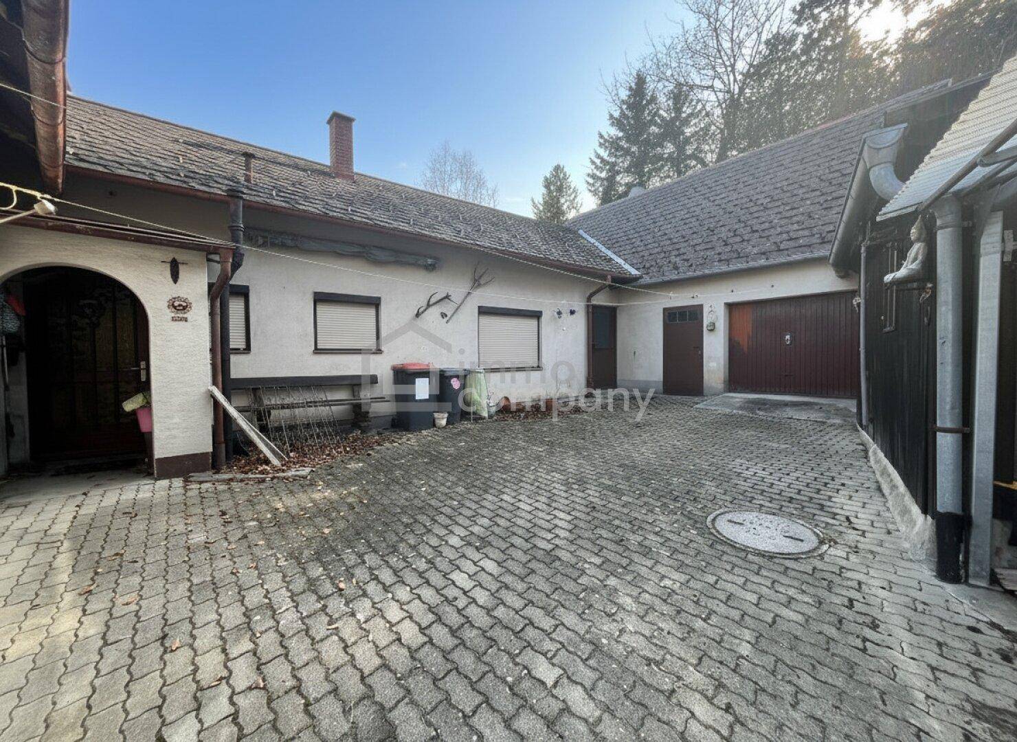 Hinterhof des Hauses mit gepflastertem Bereich, Garagen und Nebengebäuden.