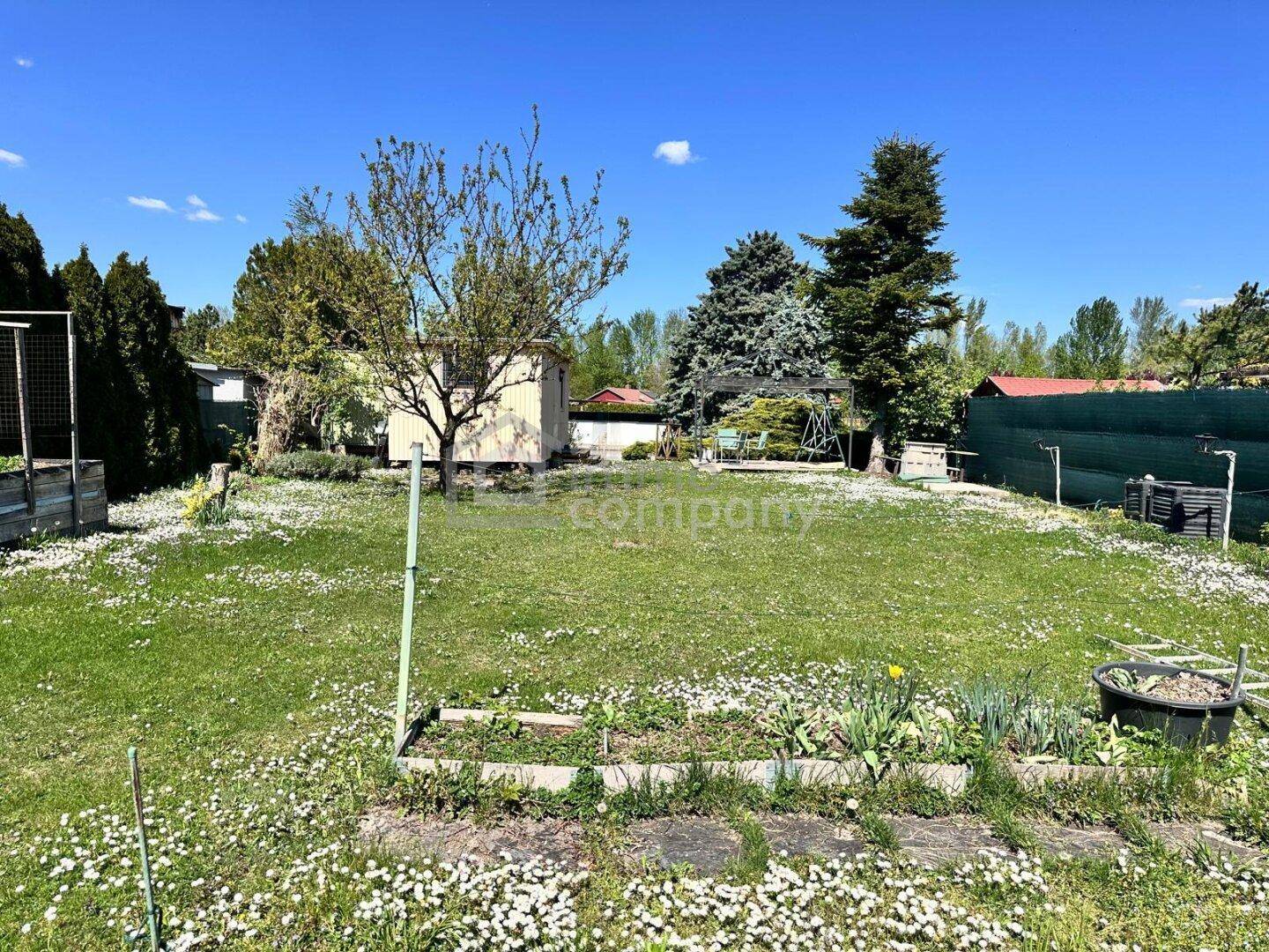 Weitläufiger Garten mit Rasenfläche, Blumenbeeten und einem kleinen Gartenhaus im Hintergrund.