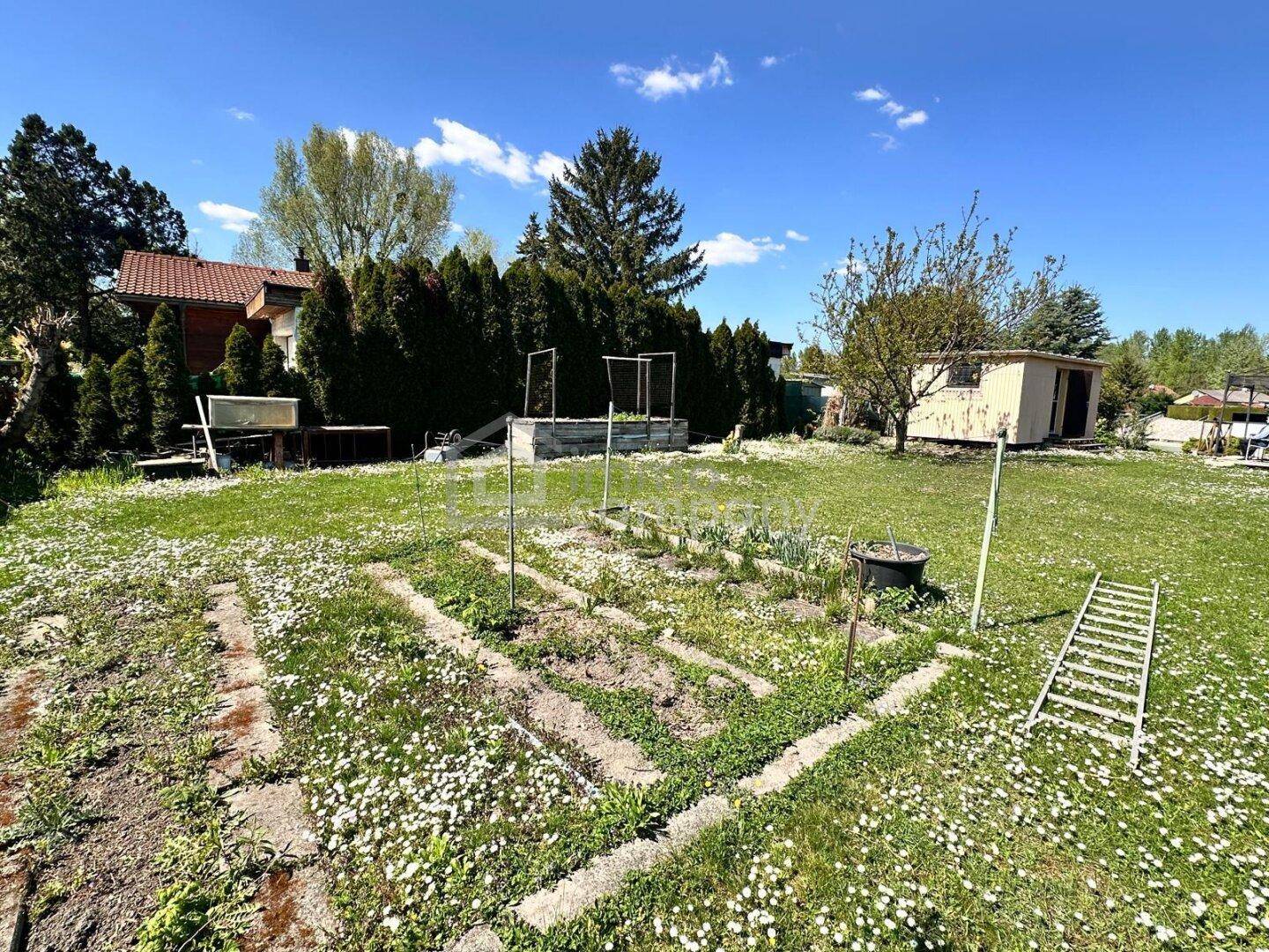 Garten mit Hochbeeten, Rasenfläche und einem Gartenhaus, ideal für den Anbau von Gemüse.