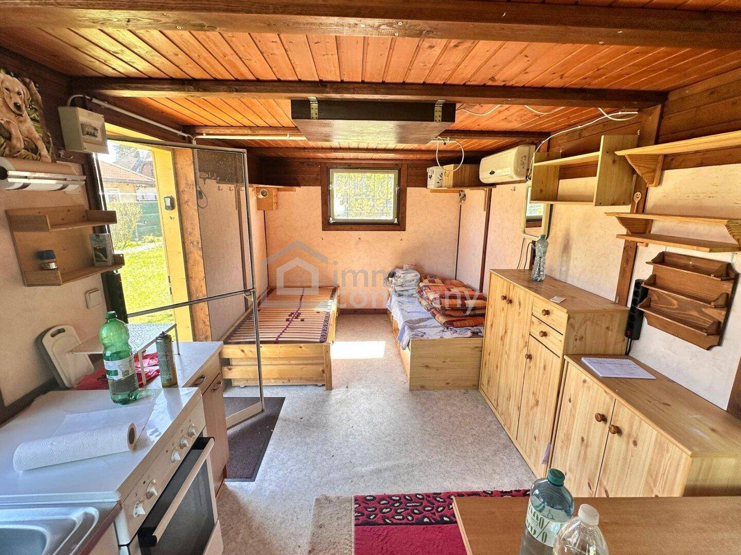 Einfacher Innenraum aus Holz mit zwei Betten und einer kleinen Küchenzeile, rustikal eingerichtet.
