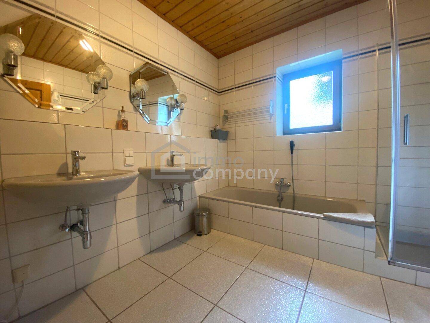 Funktionales Badezimmer mit zwei Waschbecken, Badewanne, Dusche und Fenster.