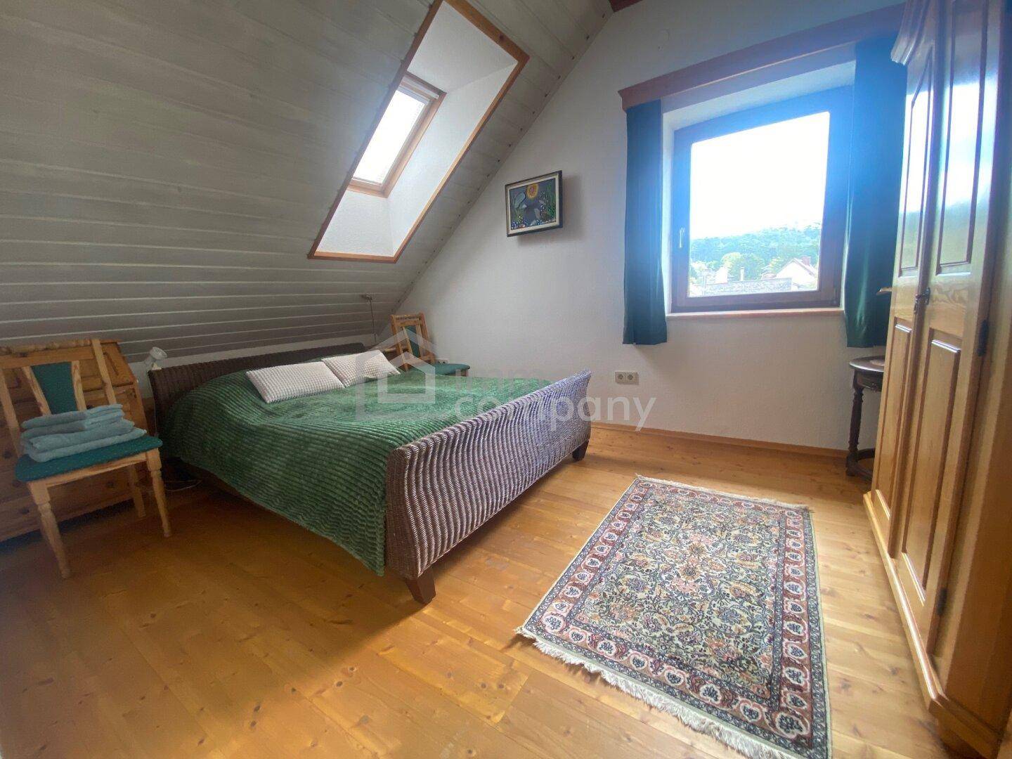 Helles Schlafzimmer im Dachgeschoss mit Holzboden, Dachfenster und schräger Decke.