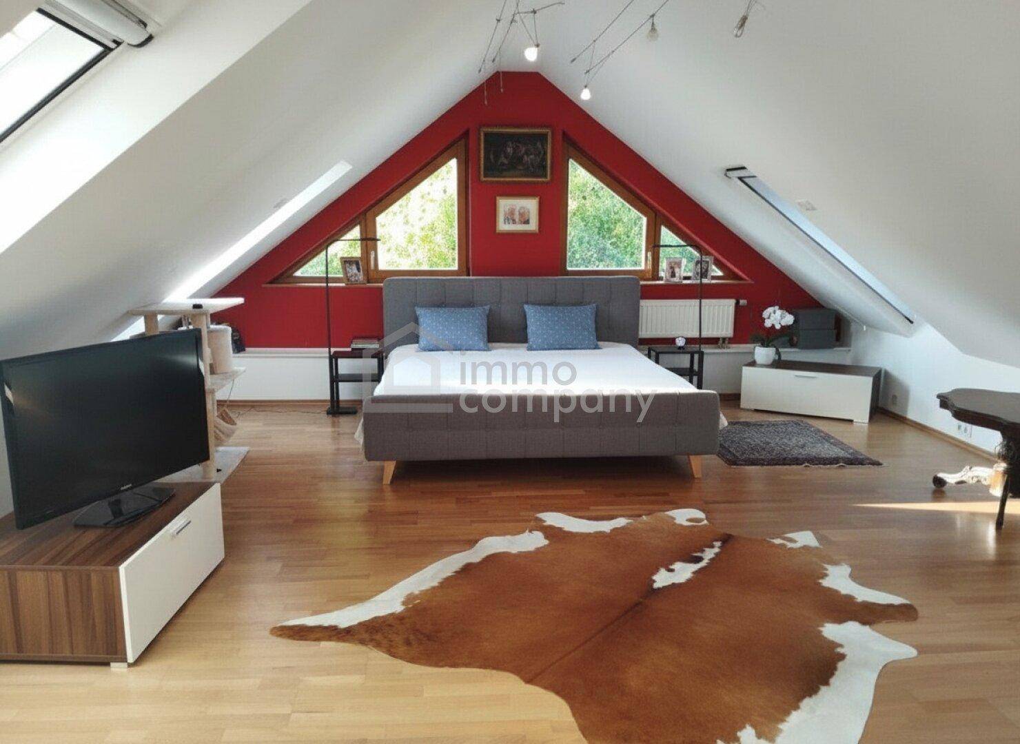 Helles Schlafzimmer im Dachgeschoss mit roten Wänden, Holzfußboden und Dachfenstern.