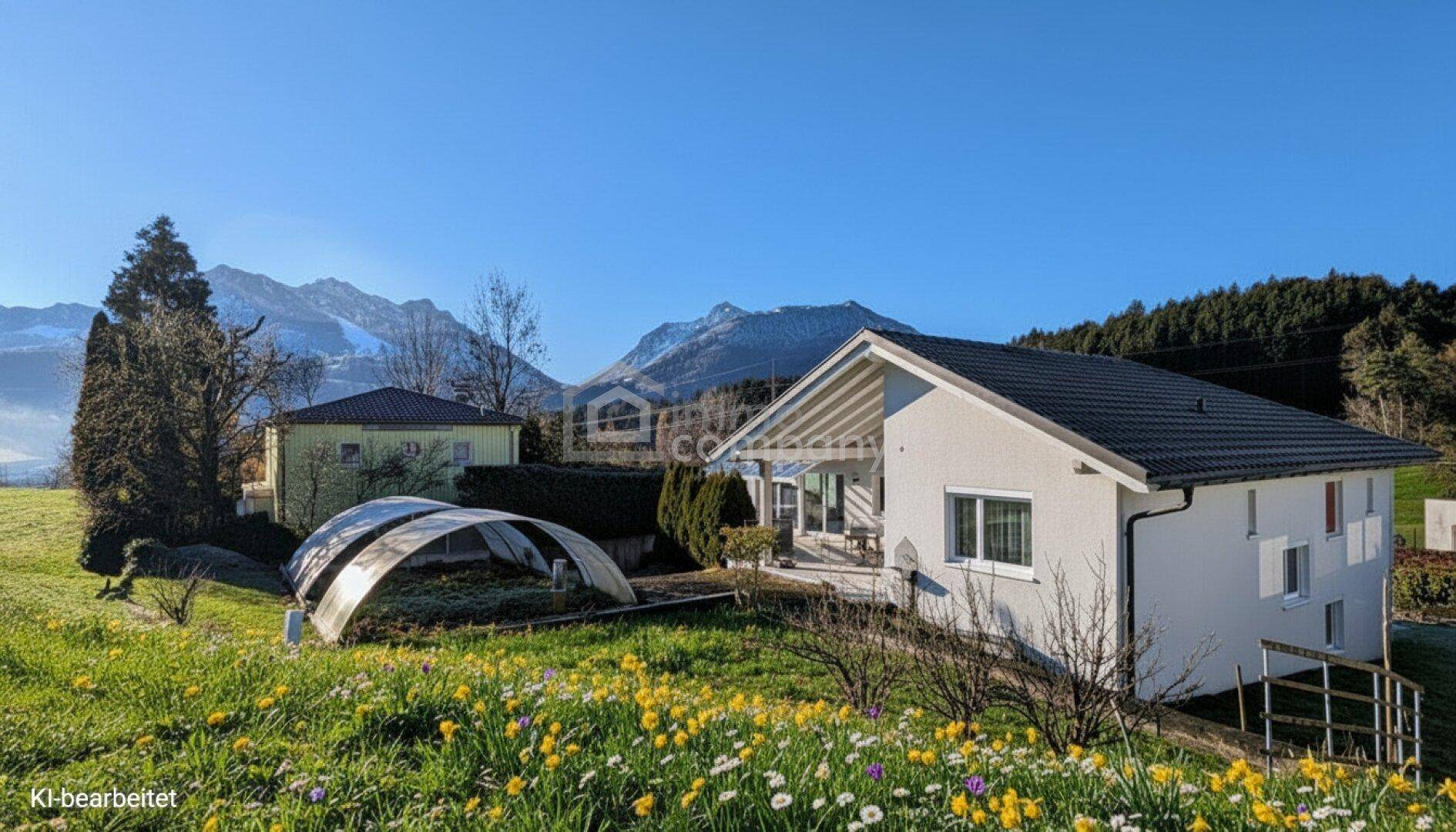 Freistehendes Haus mit blühender Wiese und Bergblick an einem sonnigen Tag.