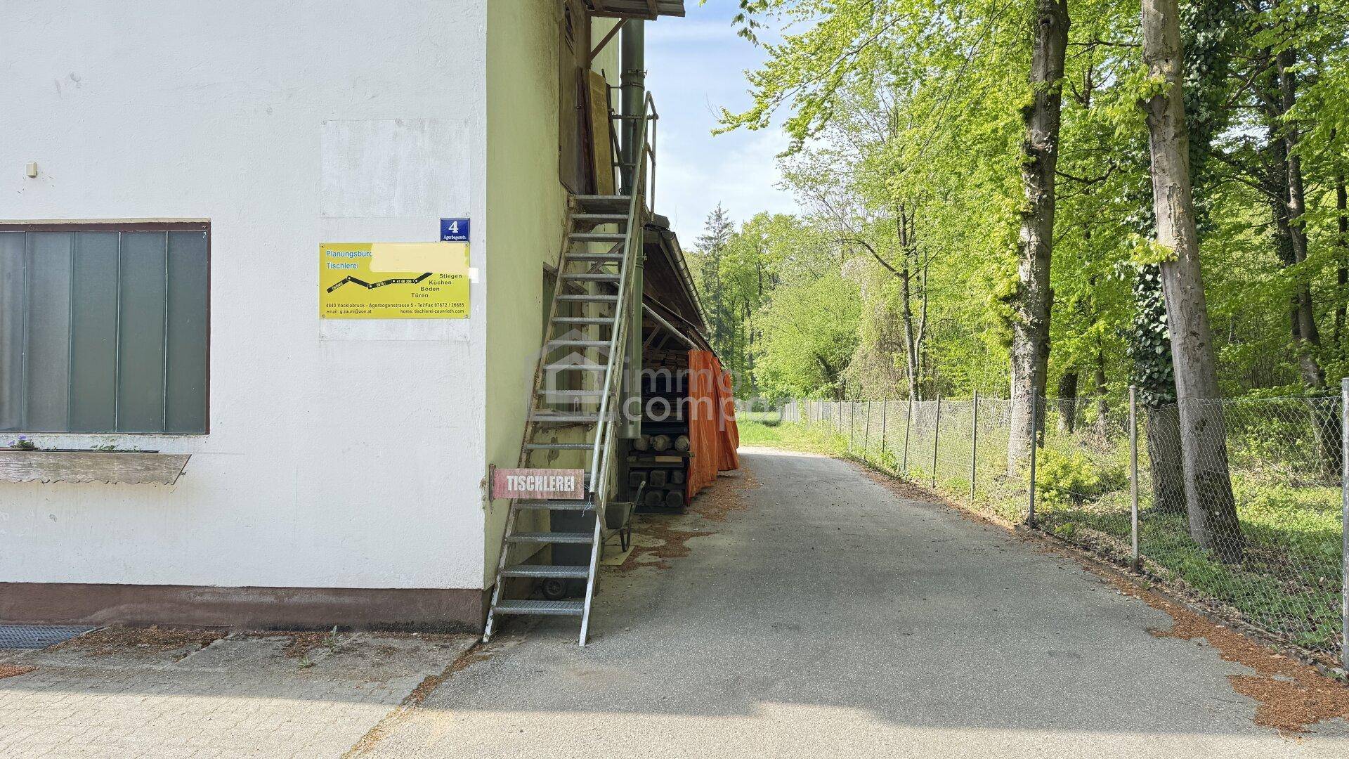 Seitlicher Zugang zum Gewerbegebäude mit Außentreppe und Blick auf den Wald.