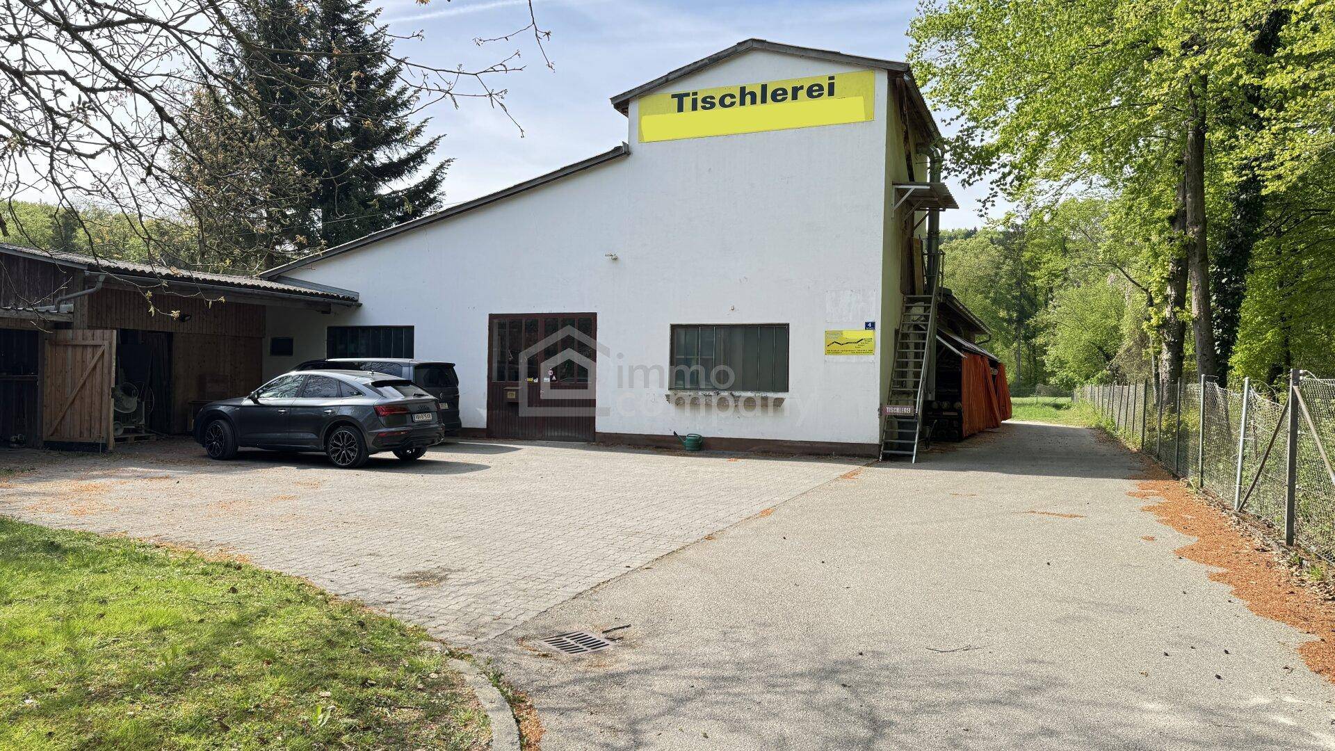 Gewerbegebäude einer Tischlerei mit großem Vorplatz und angrenzendem Waldrand.