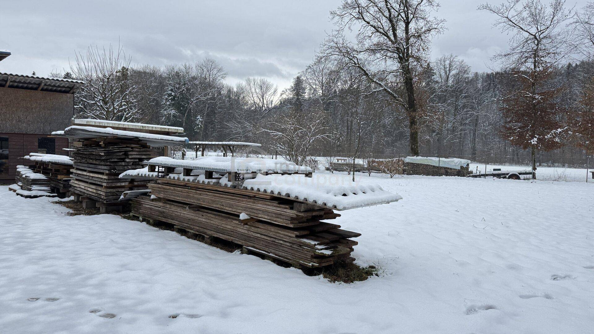 Winterlandschaft mit schneebedecktem Gelände und gestapeltem Holz im Freien.
