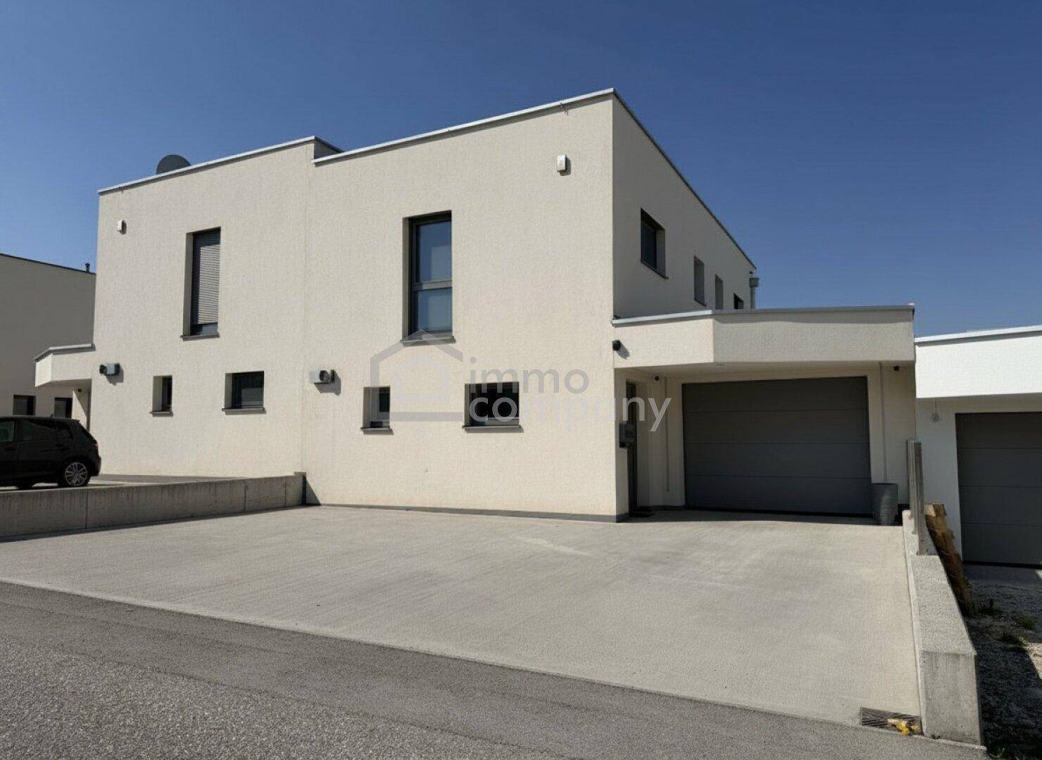 Moderne Doppelhaushälfte mit heller Fassade, Garagentor und großzügiger Auffahrt.