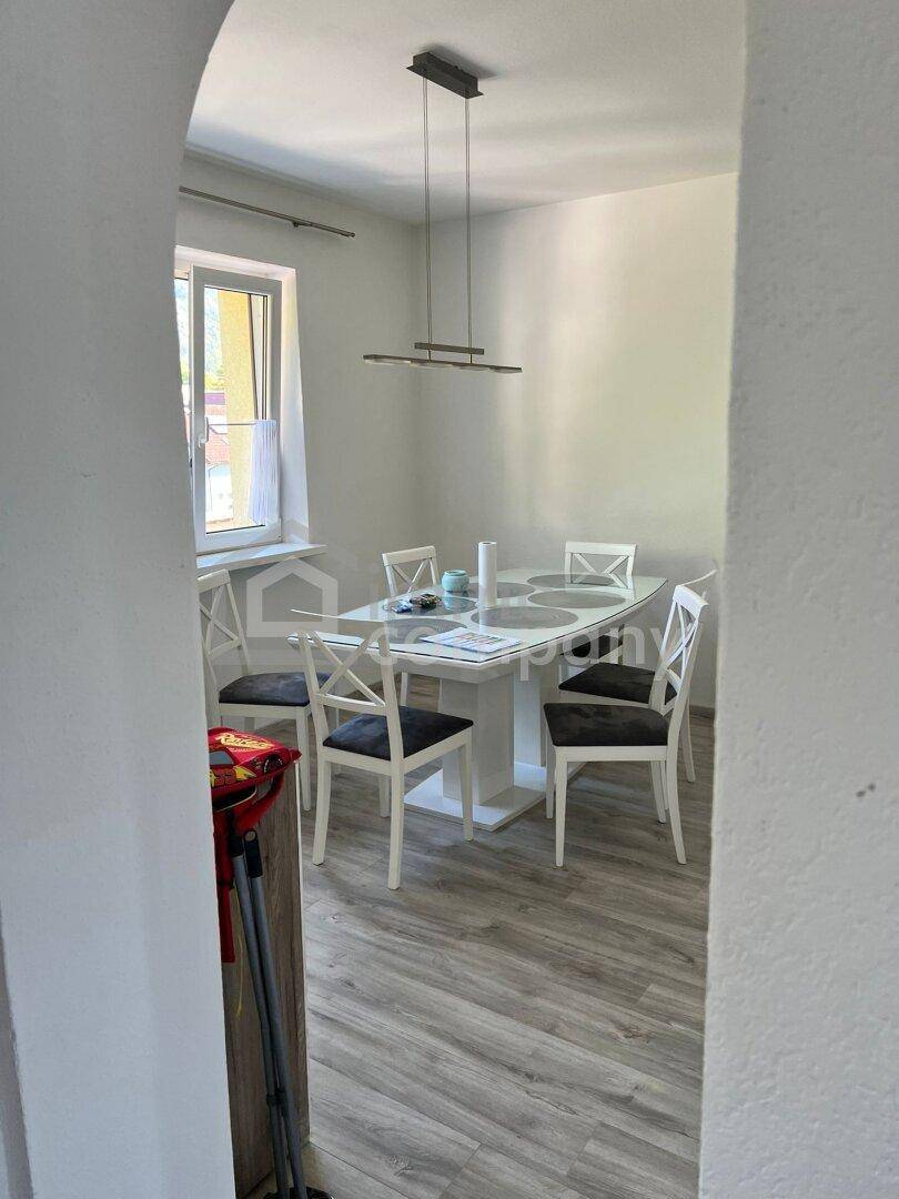 Heller Essbereich mit modernem weißen Esstisch und Stühlen neben einem Fenster.