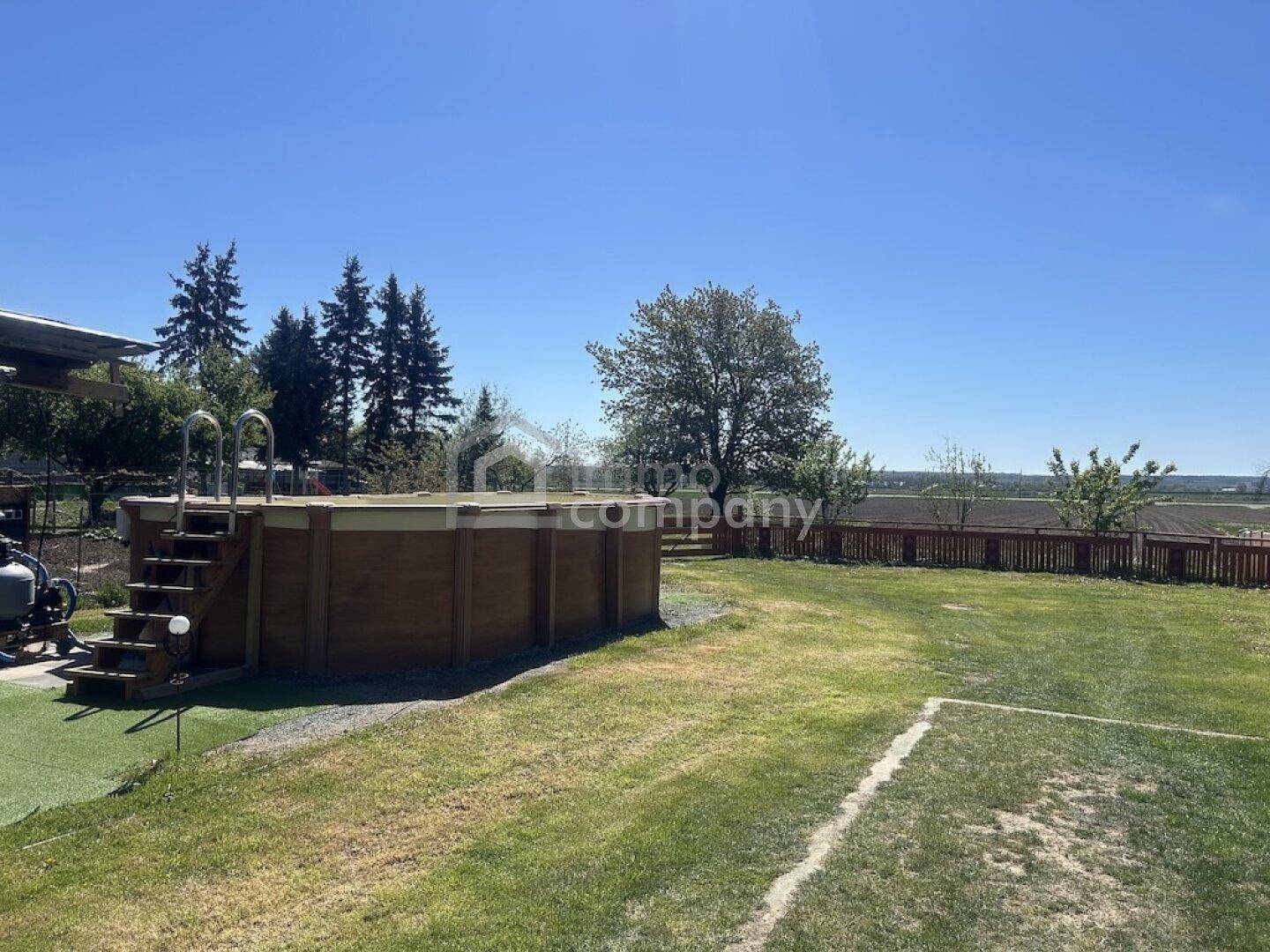 Weitläufiger Garten mit einem Aufstellpool und Rasenfläche unter klarem Himmel.