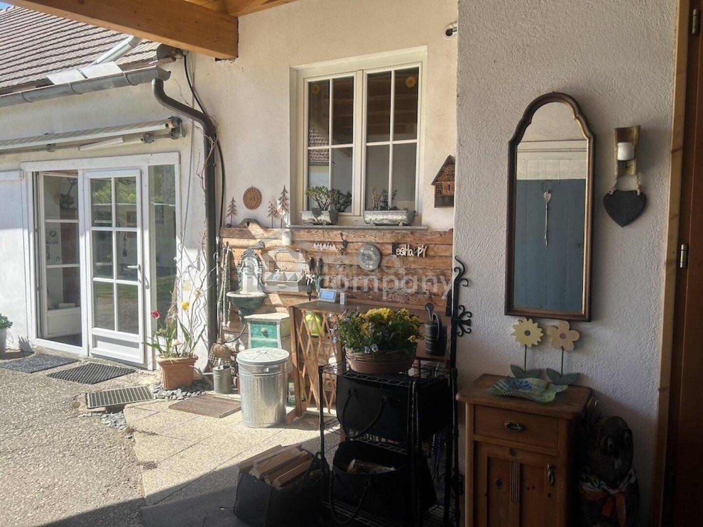 Überdachter Außenbereich mit dekorativen Elementen und Zugang zum Haus an einem sonnigen Tag.