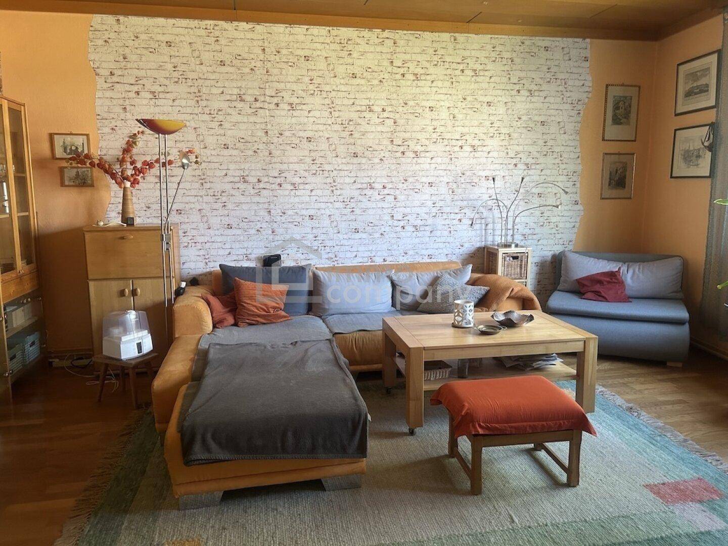 Gemütliches Wohnzimmer mit bequemer Couch, Holzboden und einer Wand mit Ziegelsteinmuster.