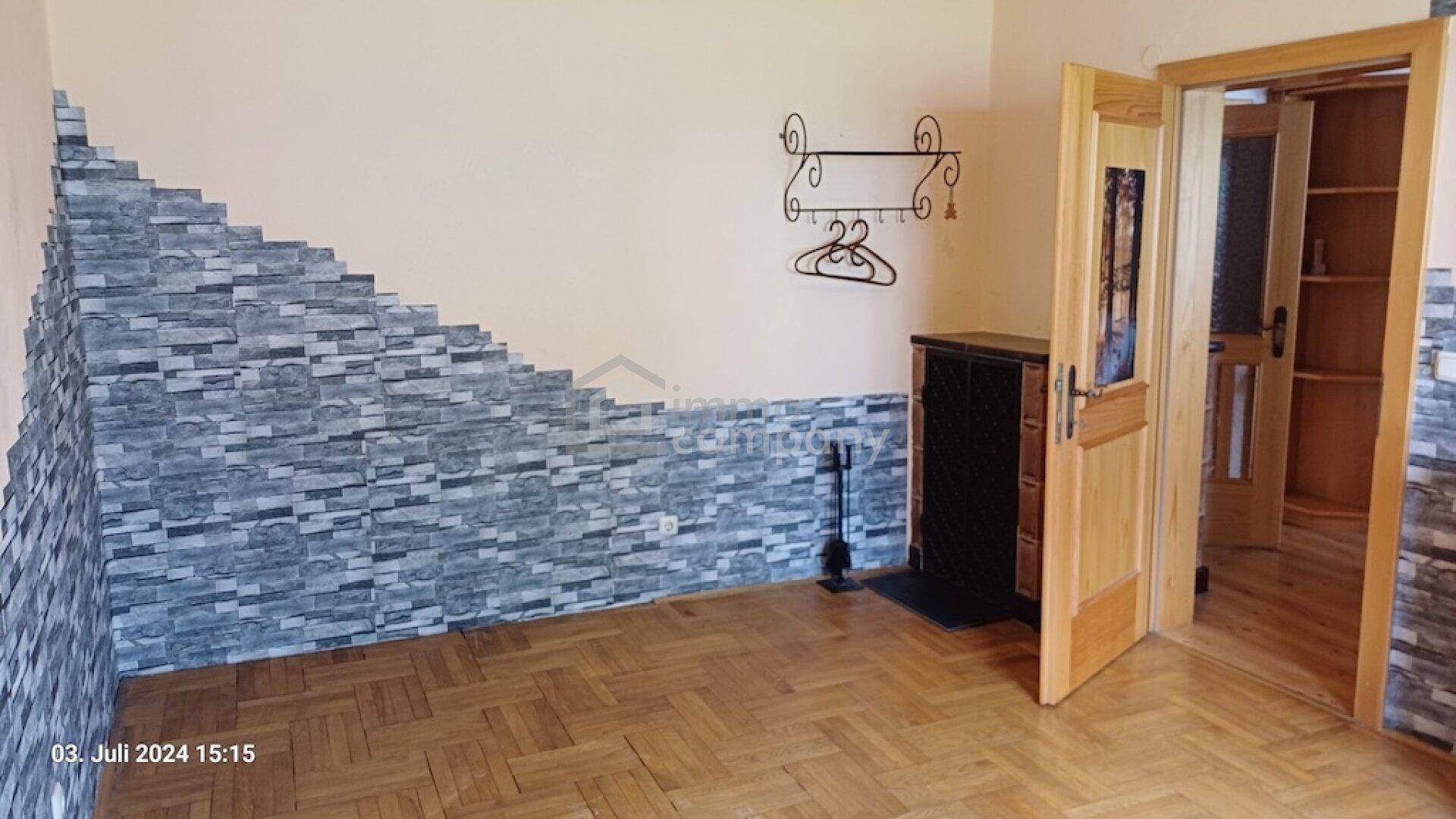 Raum mit Fischgrätparkett, dekorativer Steinwand und einem traditionellen Kachelofen.