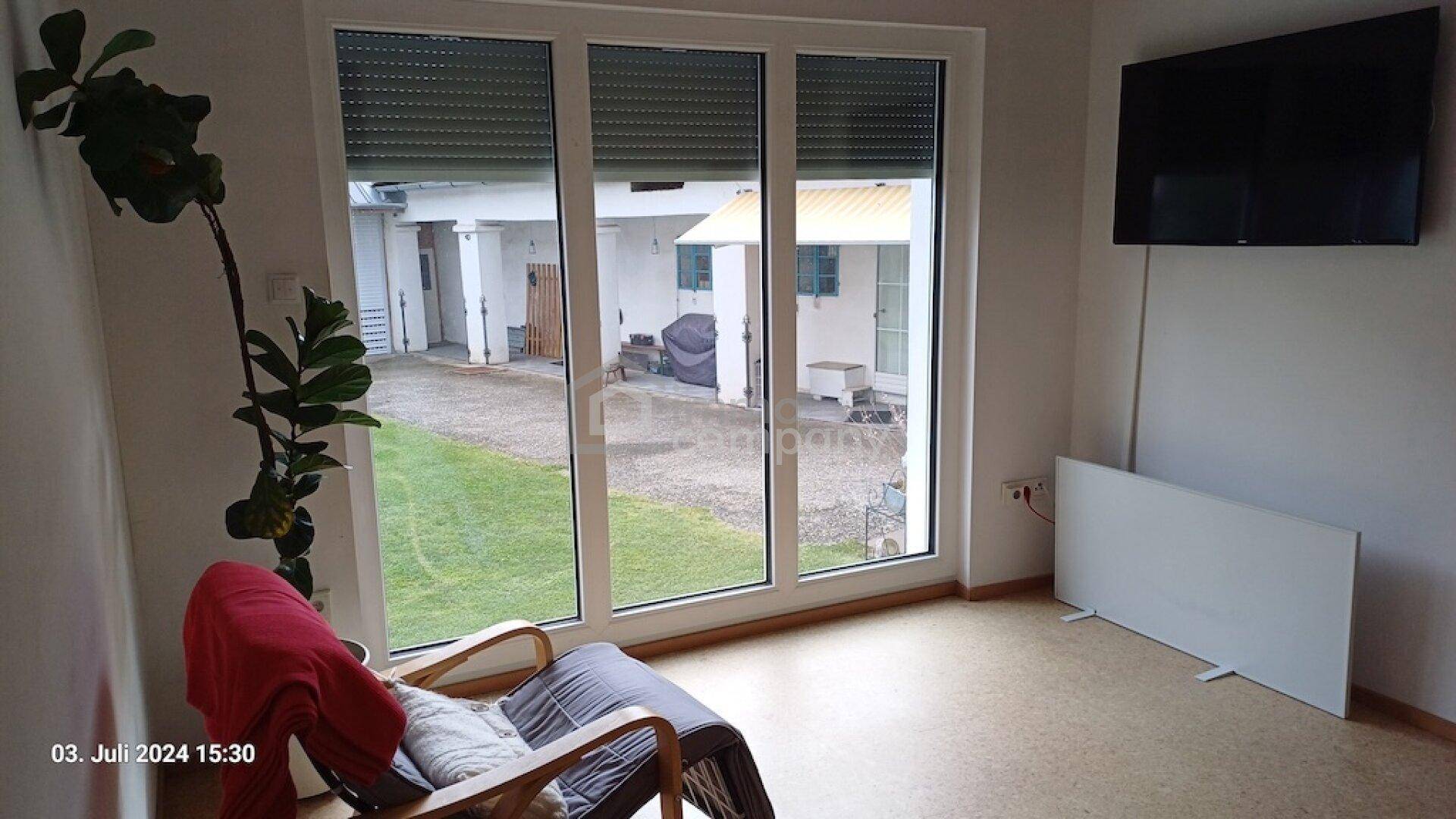 Heller Raum mit großen Fenstern, die einen Blick auf den Hof und den Garten bieten.