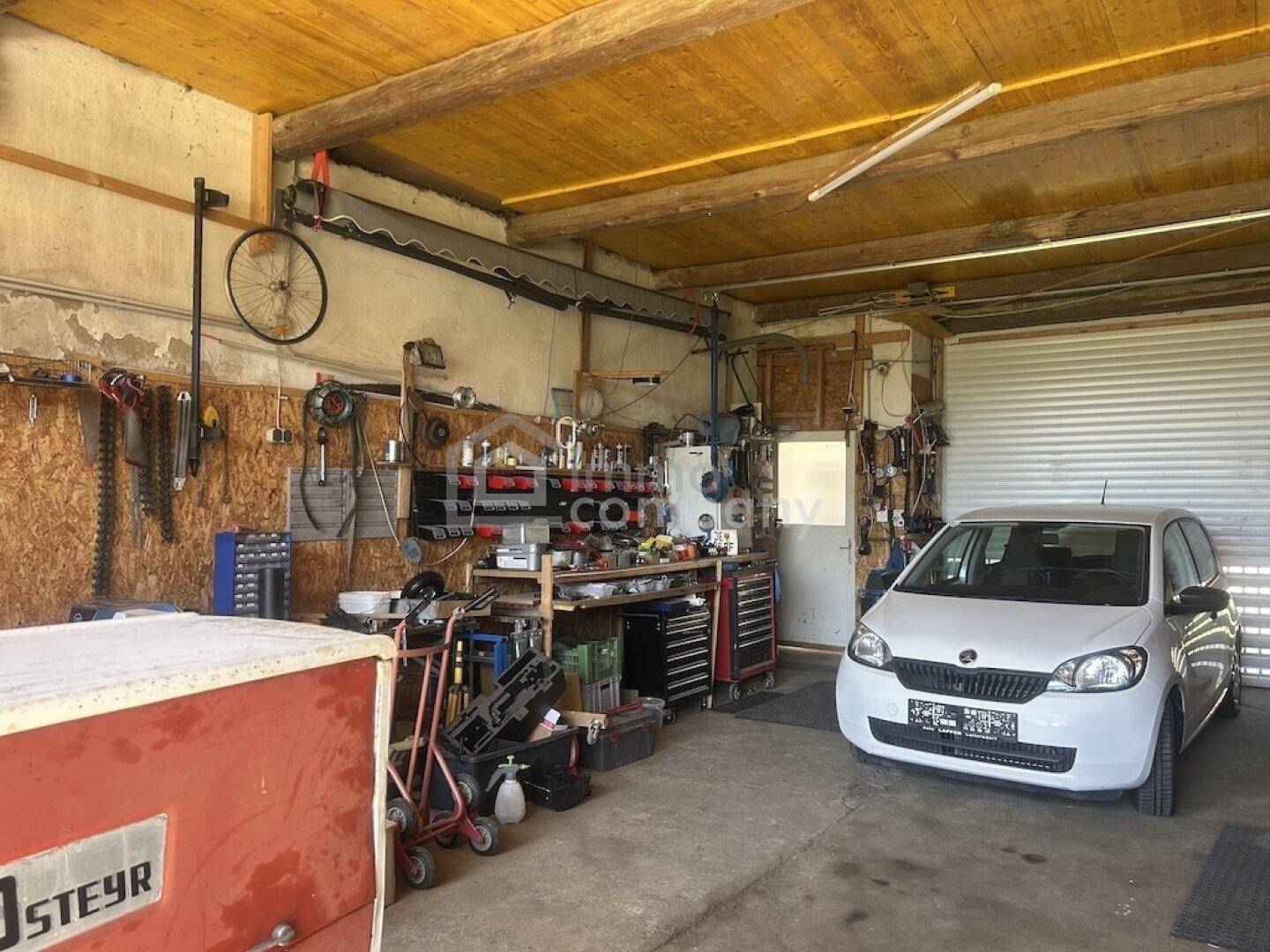 Geräumige Garage mit Werkstattbereich, vielen Werkzeugen und einem geparkten Auto.