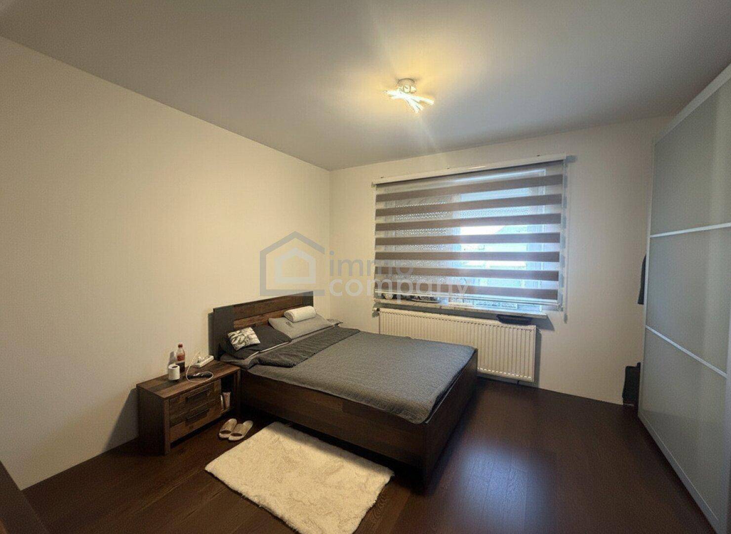 Gemütliches Schlafzimmer mit Holzbett, Nachttisch und Heizkörper unter dem Fenster.